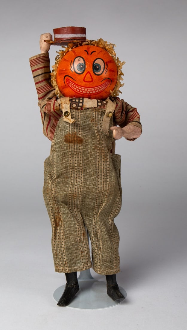 PUMPKIN HEAD HALLOWEEN SQUEEZE TOY.: PUMPKIN HEAD HALLOWEEN SQUEEZE TOY. Germany, 20th Century. Having a painted, composition head with crepe paper hair as well as wood arms and legs; tips hat when squeezed; 10.75"h. 4.25"w. Provenance: 