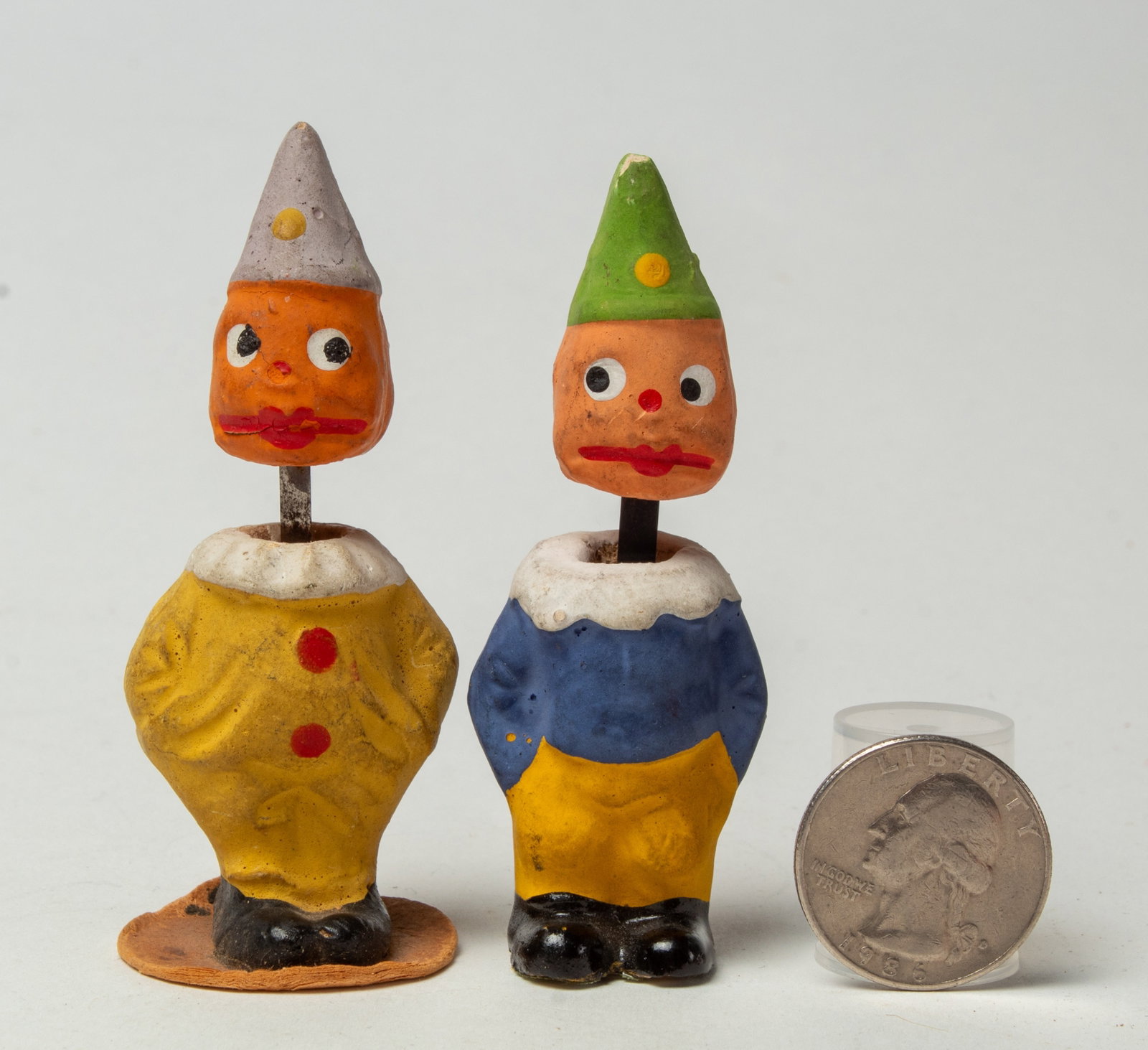 TWO DIMINUTIVE CLOWN PUMPKIN HEAD NODDERS.: TWO DIMINUTIVE CLOWN PUMPKIN HEAD NODDERS. Germany, early 20th Century. One wearing a yellow clown suit with red buttons, a white ruffled collar, and a purple dunce cap, 3"h. Together with a modder we