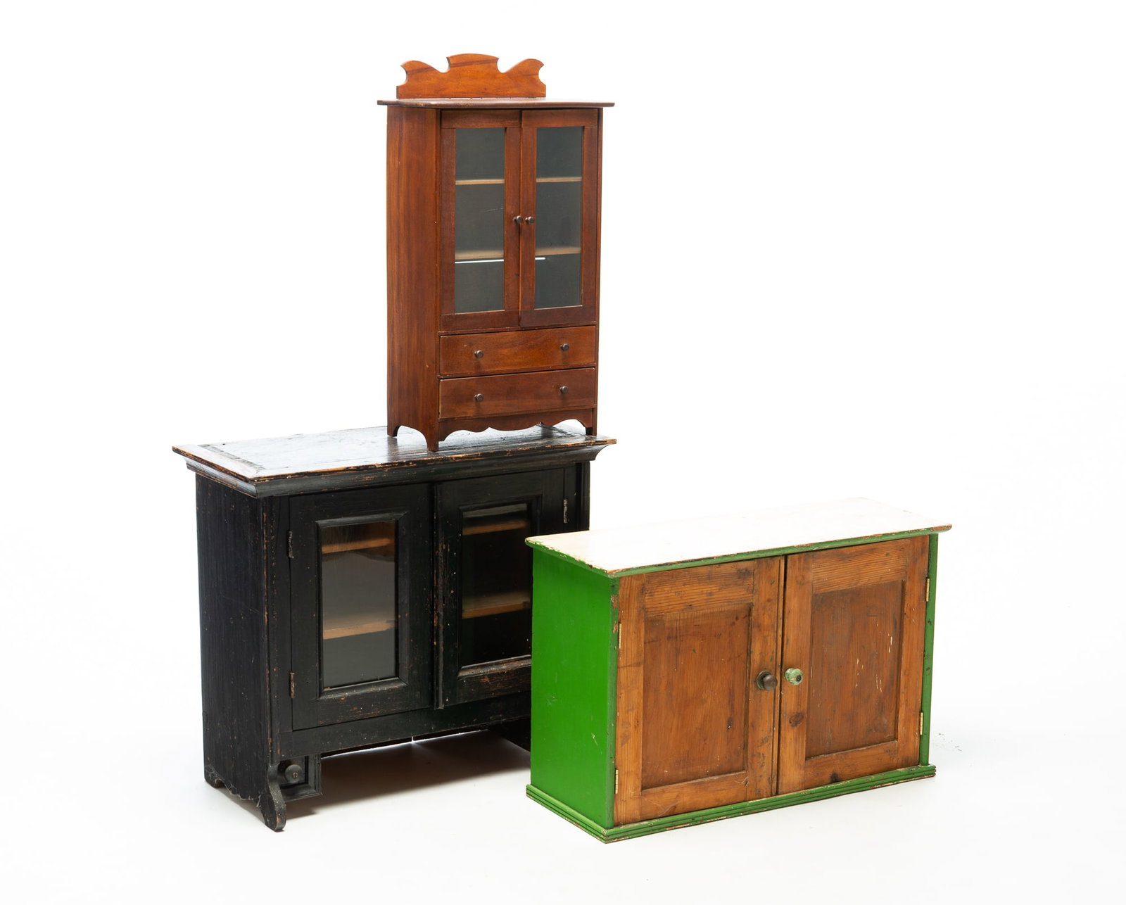 THREE DIMINUTIVE CABINETS.: THREE DIMINUTIVE CABINETS. American, late 19th or early 20th Century. A child's-size birch and pine cupboard with top applied cornice moldings, two single-pane glass doors, and two lower candle