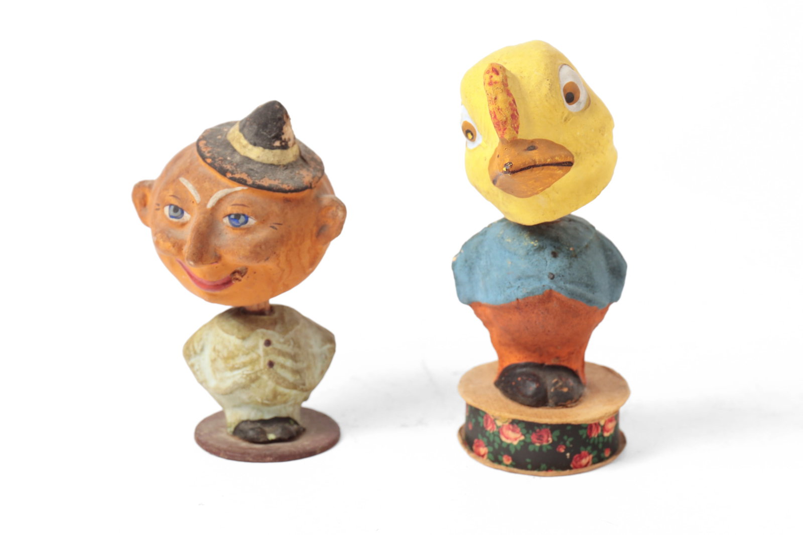TWO NODDING HEAD FIGURES.: TWO NODDING HEAD FIGURES. German, early 20th Century. A pumpkin-headed man spring nodder, with prominent ears, smoking a cigar and wearing a hat, dressed in a light green suit, standing on a circular