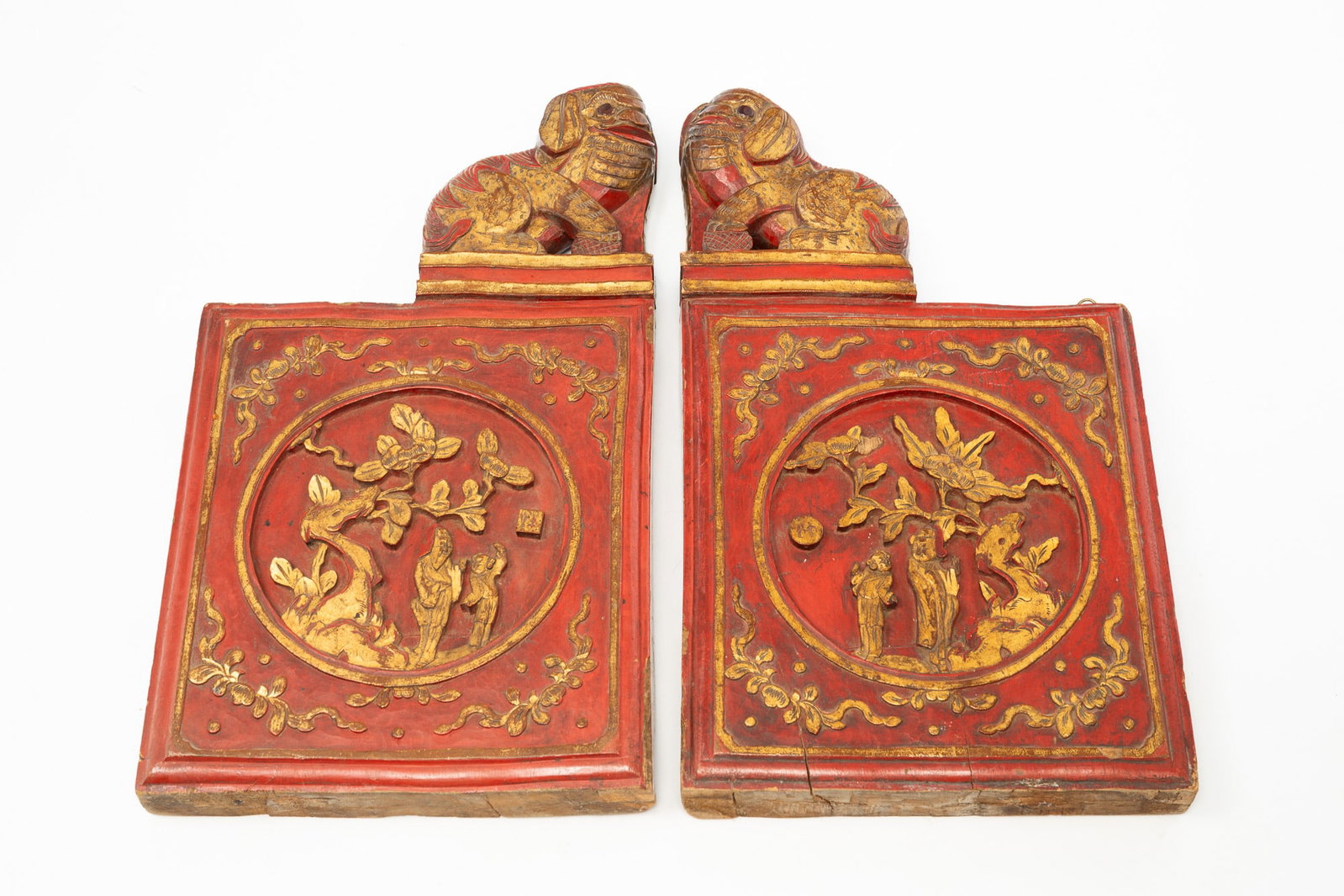 PAIR OF CHINESE CARVED, PAINTED, AND PARCEL-GILT ELM PANELS.: PAIR OF CHINESE CARVED, PAINTED, AND PARCEL-GILT ELM PANELS. 20th Century. Foo dog finials over square panels with circular reserves, carved with trees and costumed figures. Cinnabar paint with gold