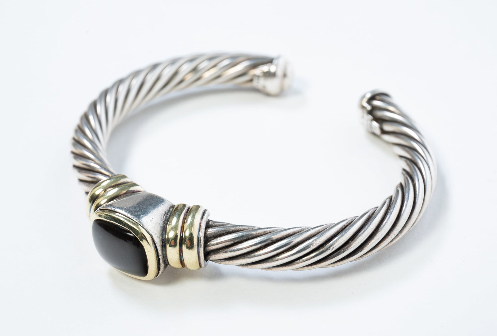 DAVID YURMAN CABLE ONYX STATION CUFF BRACELET IN STERLING SILVER.: DAVID YURMAN CABLE ONYX STATION CUFF BRACELET IN STERLING SILVER. American, contemporary. Twisted cable cuff with 14k yellow gold accents and set with a central polished onyx cabochon. 6" interior.