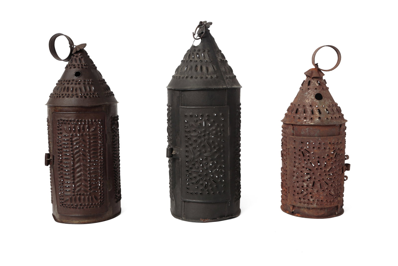 THREE PUNCHED TIN CANDLE LANTERNS.: THREE PUNCHED TIN CANDLE LANTERNS. American, 19th Century. All with ring handles, cone tops, punched designs, and single candle sockets. The tallest is painted black. Tallest, 15"h. Provenance: The