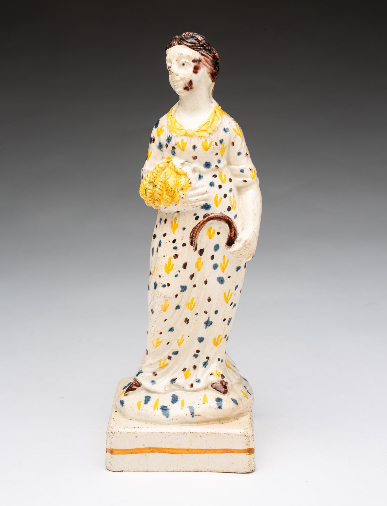 PRATTWARE ALLEGORICAL FIGURINE OF AUTUMN.: PRATTWARE ALLEGORICAL FIGURINE OF AUTUMN. English, early 19th Century . Polychrome-painted pottery figurine of a woman with long brown hair, wearing a polka-dotted dress and holding a sheaf of wheat
