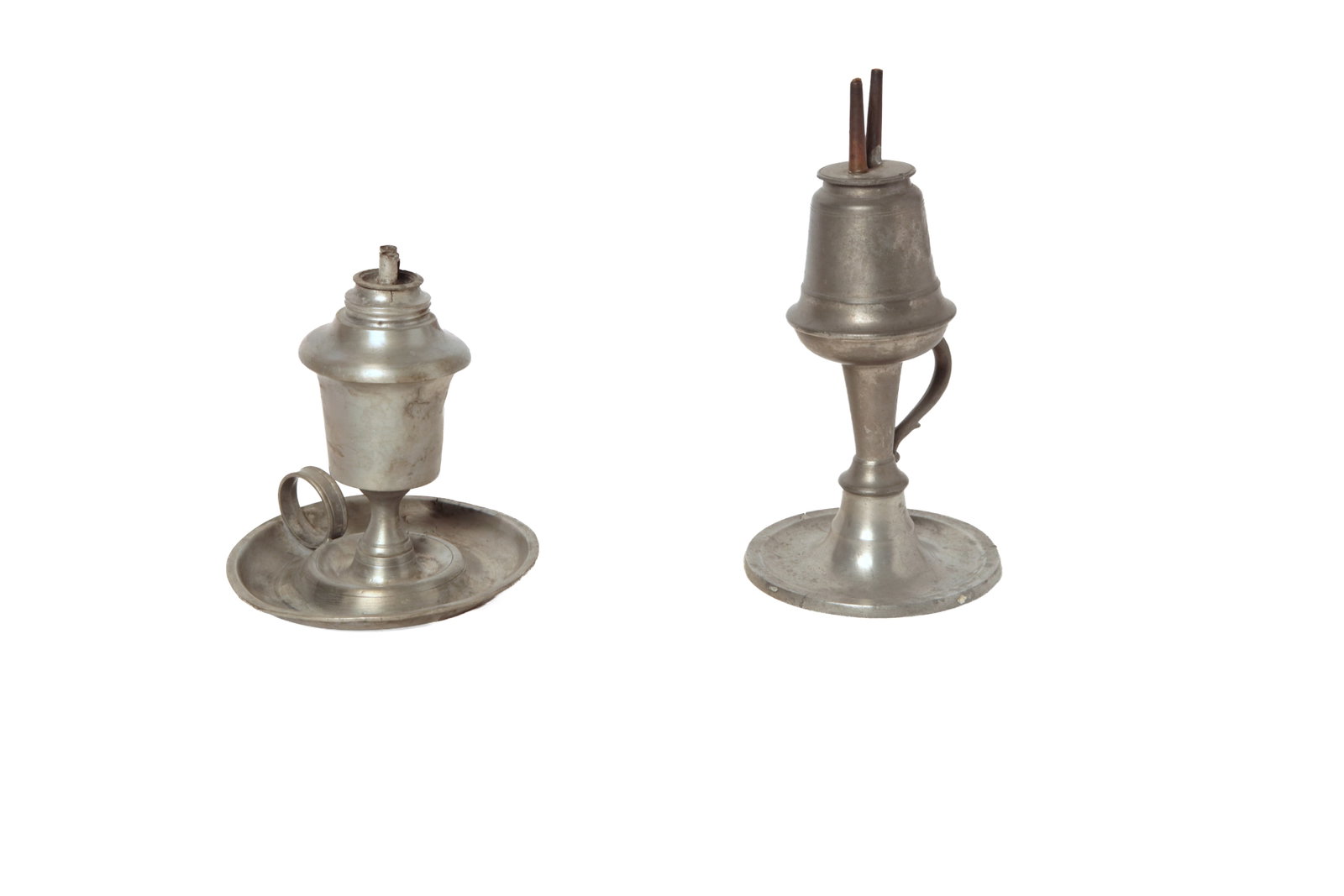 TWO PEWTER LAMPS WITH HANDLED SAUCER BASES.: TWO PEWTER LAMPS WITH HANDLED SAUCER BASES. American, 19th Century. Tallest with round base, attached handle at stem, and a camphene burner, 7.5"h., together with an acorn font, saucer base with ring