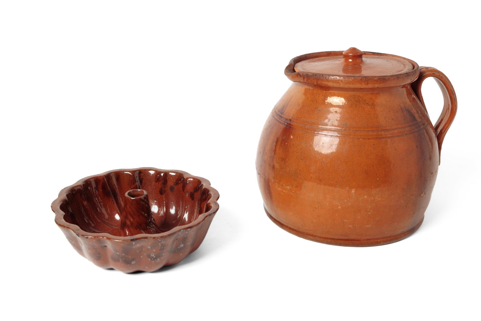 GLAZED REDWARE BATTER JUG AND TURK'S HEAD FOOD MOLD.: GLAZED REDWARE BATTER JUG AND TURK'S HEAD FOOD MOLD. American, 19th Century. Batter jug with lid, strap handle, tooling at shoulder, and an allover pumpkin glaze with manganese trails. 9"h. 9"w.