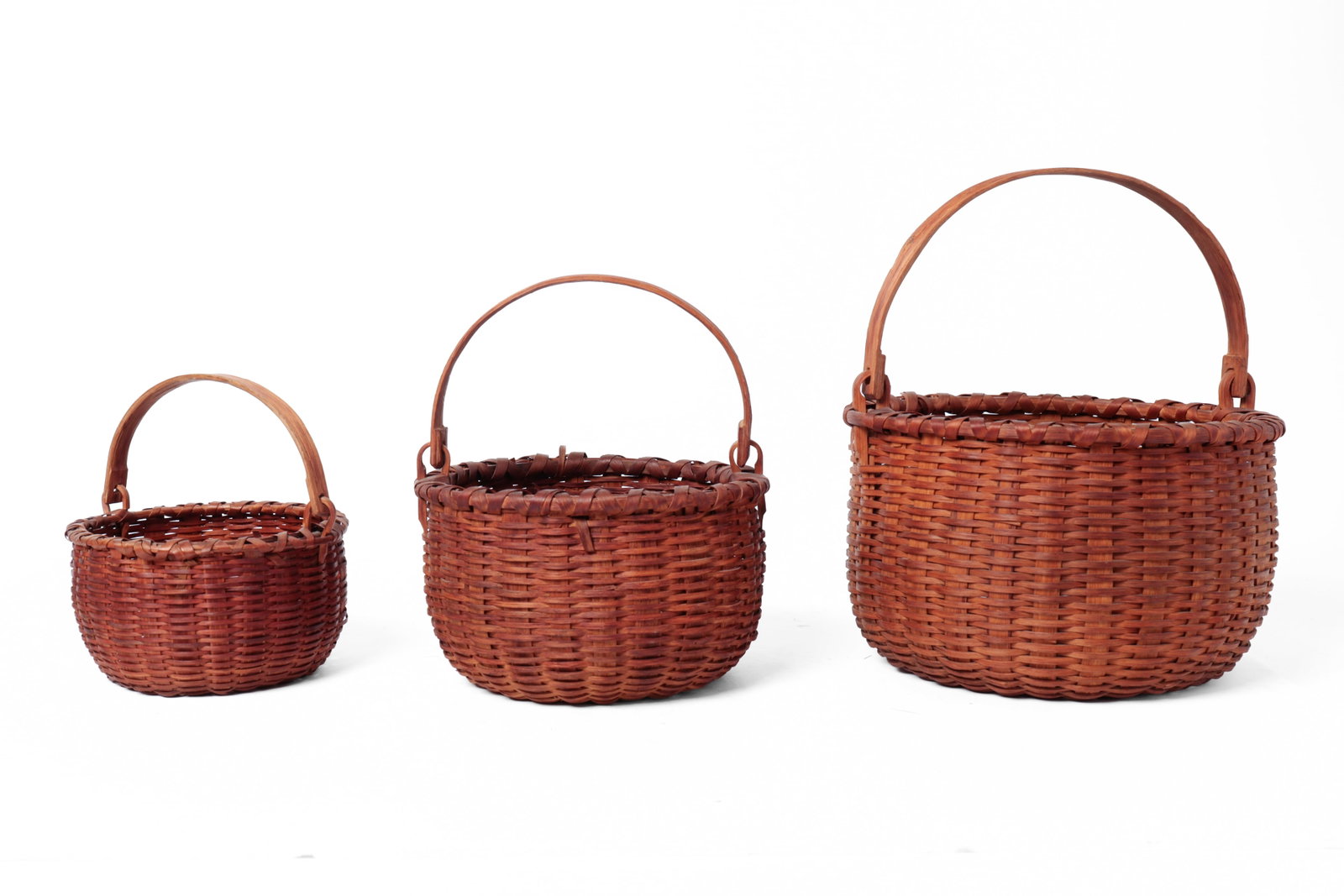 SET OF THREE NESTING SWING HANDLED BUSHWACKER BASKETS.: SET OF THREE NESTING SWING HANDLED BUSHWACKER BASKETS. American (New York), late 19th or early 20th Century. Three circular-form baskets, tightly woven splints, demi-john bottoms, wrapped rims, and la