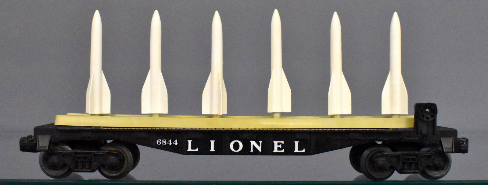 Lionel postwar O gauge 6844 missile carrying flat car: Car has light run time and is C8 with perfect lettering on both sides and six original missiles. The base that thew missiles sit on is mottled gray and tan.