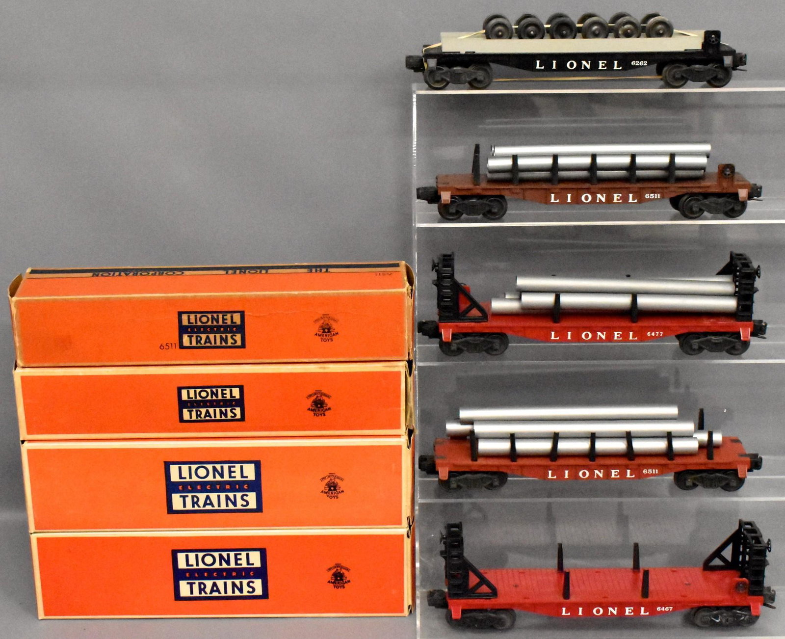 Five Lionel postwar O gauge flat cars with four: Includes two different 6511 with pipes, 6262 wheel car and two 6467 miscellaneous cars, C7 with four good to very good original boxes.