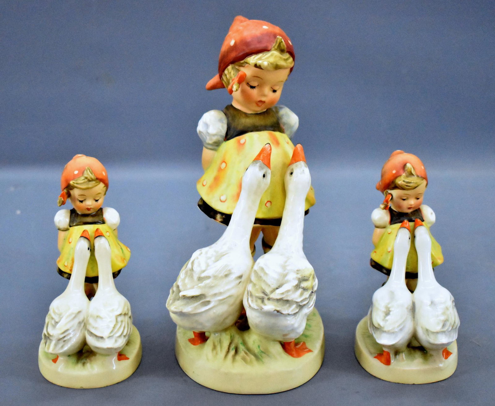 Three different Hummel 47 Goose Girl figurines: Three different Hummel 47 Goose Girl figurines, two are small with full bee and one has a tall clump of grass between the geese and the other is a 7 1/2" tall example from the laste 1970's or 80's. Al