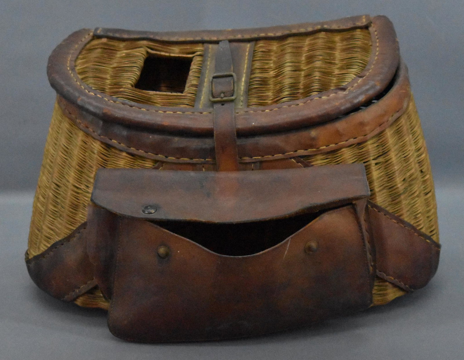 Unmarked antique wicker fishing creel: Unmarked antique wicker fishing creel. Decent condition but has a tear to the leather pouch on one side and some damaged wicker along the bottom as seen in the photos. It still displays very nicely.