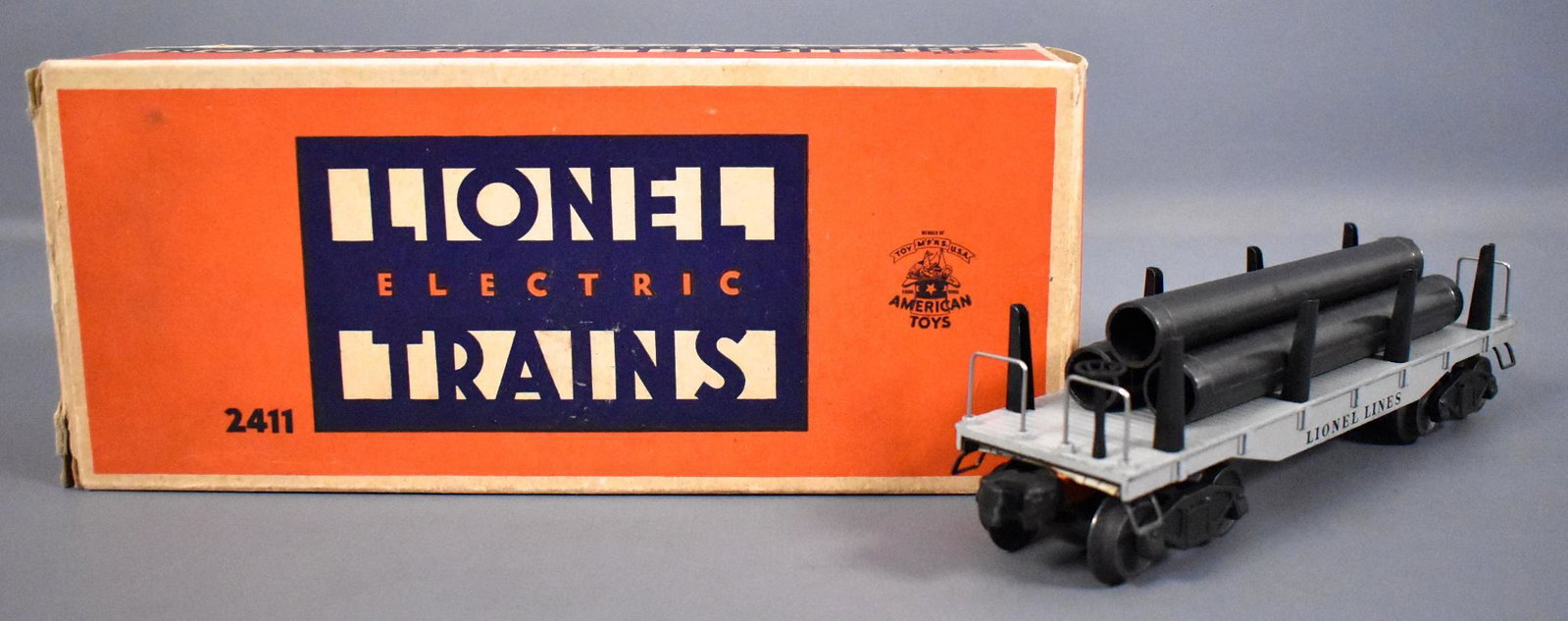 Lionel postwar O 2411 flat car with metal pipes in: Lionel postwar O 2411 flat car with metal pipes in original box. The car has very little to no run time but does have a small amount of surface paint missing from raised edges, one of the pipes is ori