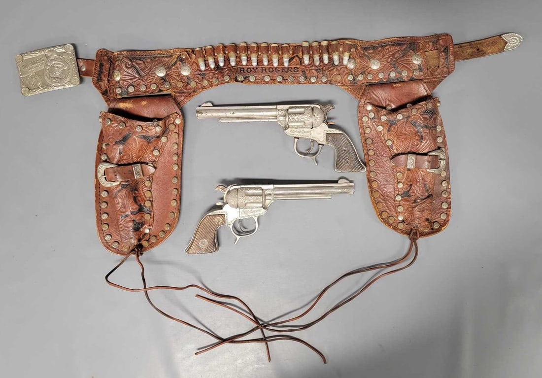 Schmidt Roy Rogers double cap gun and holster set: Schmidt Roy Rogers double cap gun and holster set, the holster has seen play time with a few of the wooden bullets missing and some rust on some of the tin buttons. The cap guns are intact but a lot o