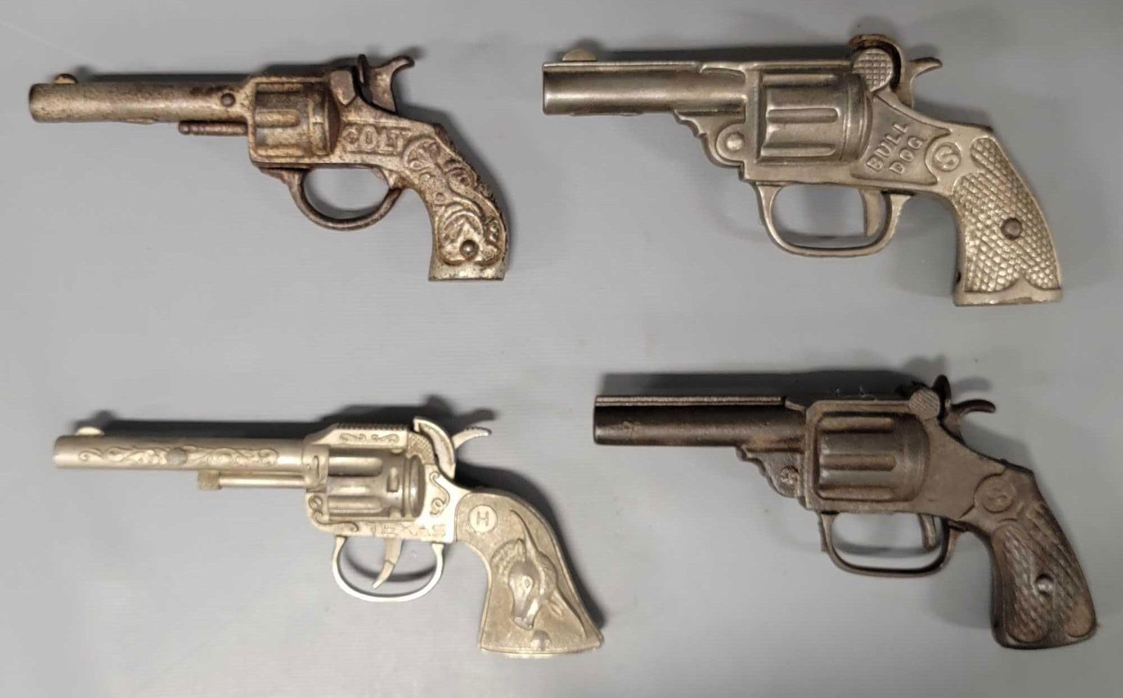 Four vintage and antique cap guns: Four vintage and antique cap guns to include cast iron Colt by Stevens, Bull Dog and unnamed with SHRINK WRAP on the handle plus a die cast Texas by Halco. All in various conditions as seen in the pho