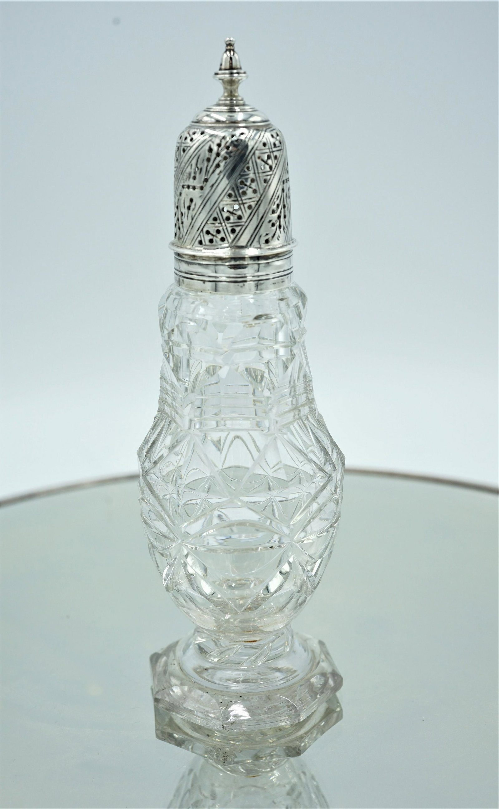 GEORGE III PERIOD MUFFINEER W/ SILVER COVER - ENGLISH: A crystal muffineer with a silver engraved cover CIRCA 1770 England. facet cut bottle with polished base. Cap has fine finial and engraving around the confectionery holes. no signatures or hallmarks n