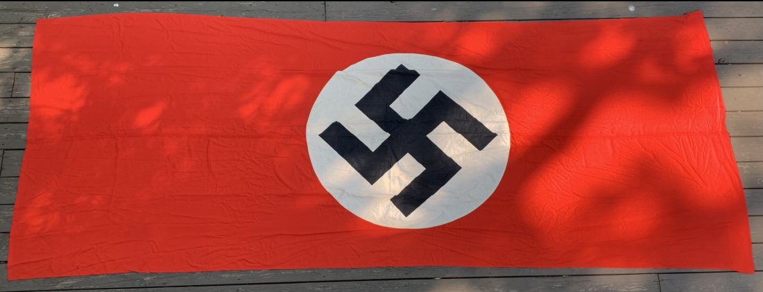 NSDAP BANNER OR FLAG FOR CELEBRATIONS. SIZE 145" x 59": Nice NSDAP banner of flag to be used during special events such as celebrations. Central white disc sewn to a red flag. Black swastika printed inside the disc. Minor staining and wear. Roughly 145" x 
