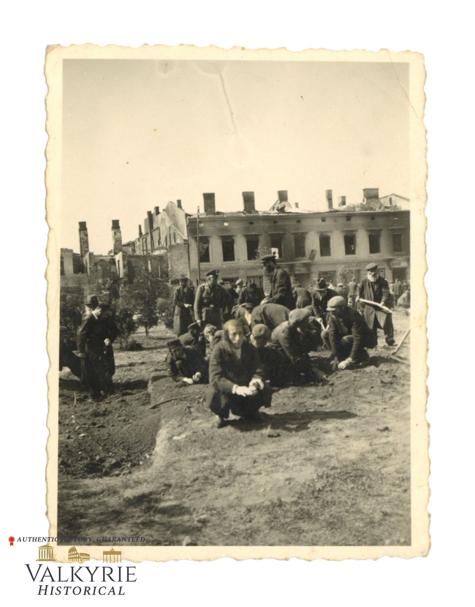 Photo of Polish Jews Forced to do Denigrating Works in an Unknown Jewish Ghetto: Photo of Polish Jews Wearing the David Star Armband Forced to do Denigrating Works. Some are working with a shovel, others are working with bare hands on the ground. We can see also a German officer o
