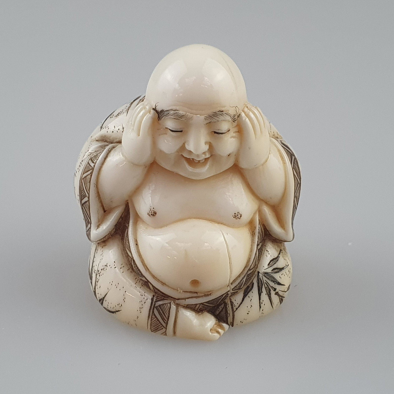 Shunga-Netsuke - Japan, ca. Taishō-/ frühe Shōwa-Zeit, feine Elfenbein-Schnitzarbeit: Shunga-Netsuke - Japan, ca. Taishō-/ frühe Shōwa-Zeit, feine Elfenbein-Schnitzarbeit mit gravierten und akzentuierten Details, Katabori, der Glücksgott Hotei, sich verschmitzt l