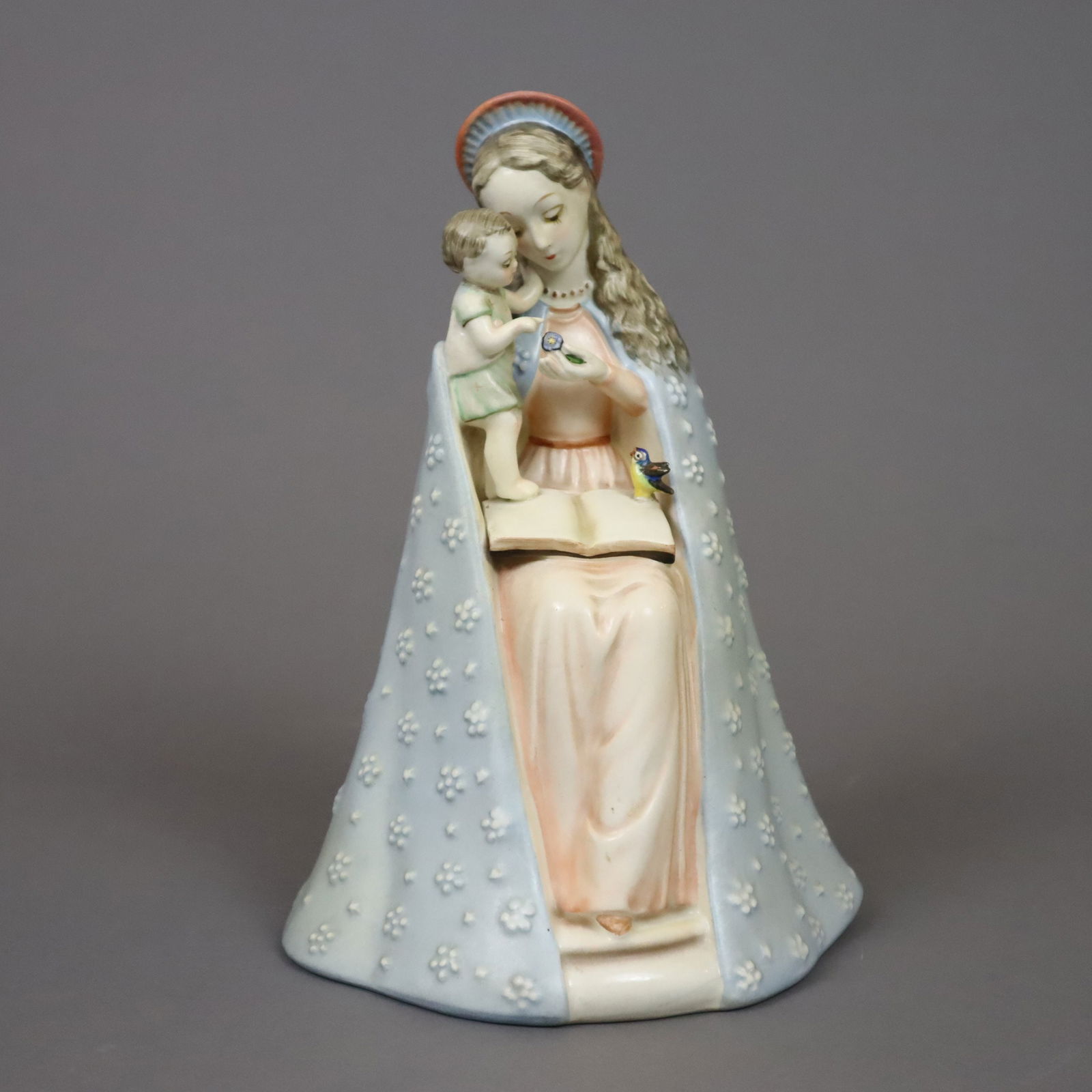 Hummelfigur "Blumenmadonna" - Goebel, 2. Hälfte 20. Jh., Ent: Hummelfigur "Blumenmadonna" - Goebel, 2. Hälfte 20. Jh., Entwurf: Reinhold Unger 1935, Modellnr. 10/1, Feinsteingut, farbig bemalt, sitzende Madonna mit Heiligenschein, der weite Umhang blumenrel