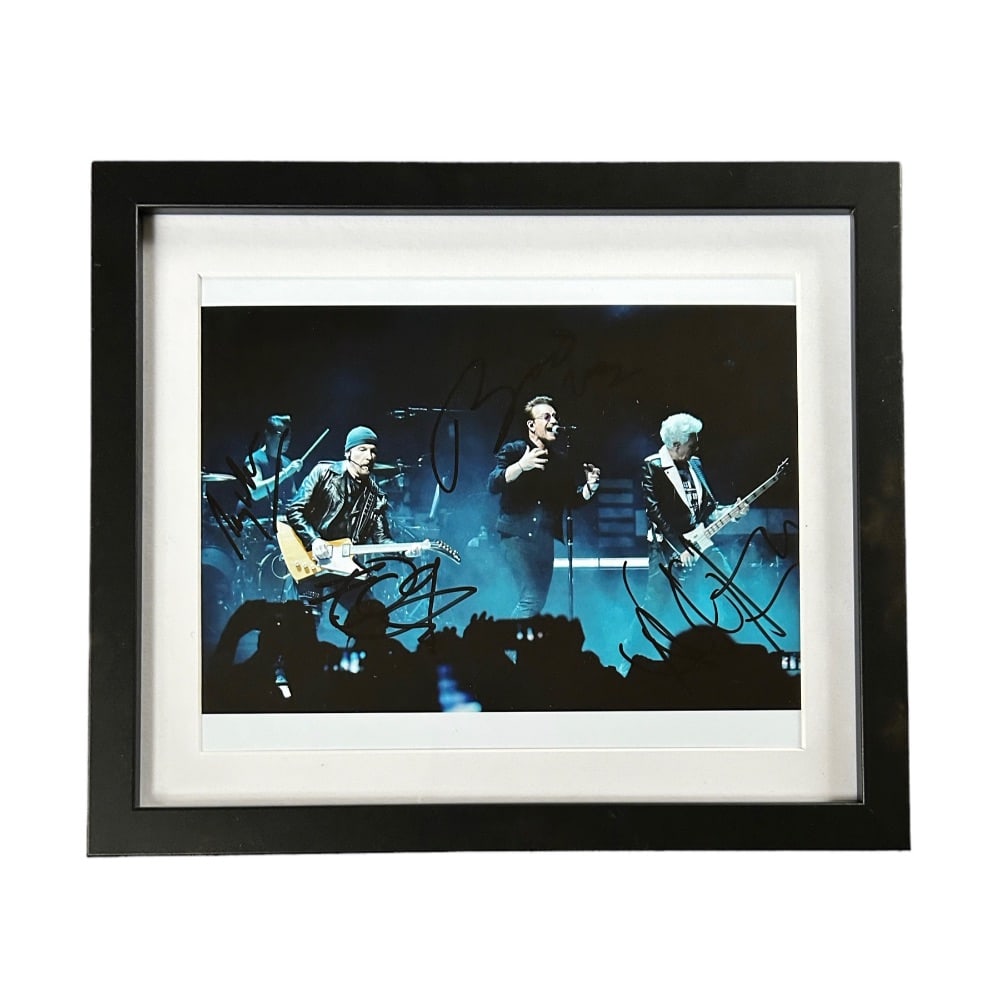 U2 Fully Signed Framed Photograph: This lot is a framed 10x8" print autographed by Bono, The Edge, Larry Mullen Jr. and Adam Clayton of U2. The photo is housed within a mounted black wooden frame, an ideal display item for collectors. 