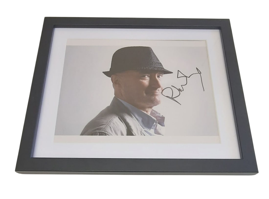 Phil Collins Signed Framed Photograph: This lot is a framed 10x8" photograph, autographed by Phil Collins. The photo is housed within a mounted black wooden frame, an ideal display item for collectors. Item comes with third-party authentic
