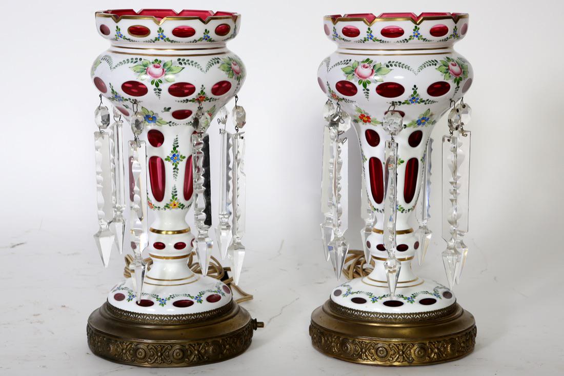 Pair of Bohemian Cut Glass Cranberry Mantle Lusters: Pair of electric Bohemian white cased cut glass to cranberry glass mantle lusters with enameled floral decoration with cut glass spear prisms. Condition:Good,one small top rim chip,typical minor knick