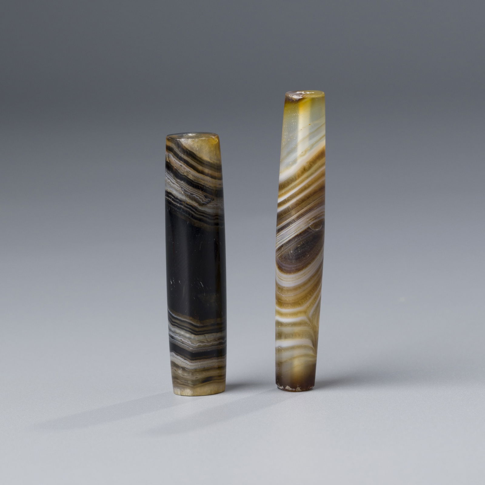TWO LARGE WESTERN ASIATIC BANDED AGATE BEADS, 1ST MILLENNIUM BC [22G]: A pair of large banded agate beads from Western Asia, dating to the 1st millennium BC. Weighing a combined 22 grams, these beads feature striking natural banding and finely shaped forms.*If you win th