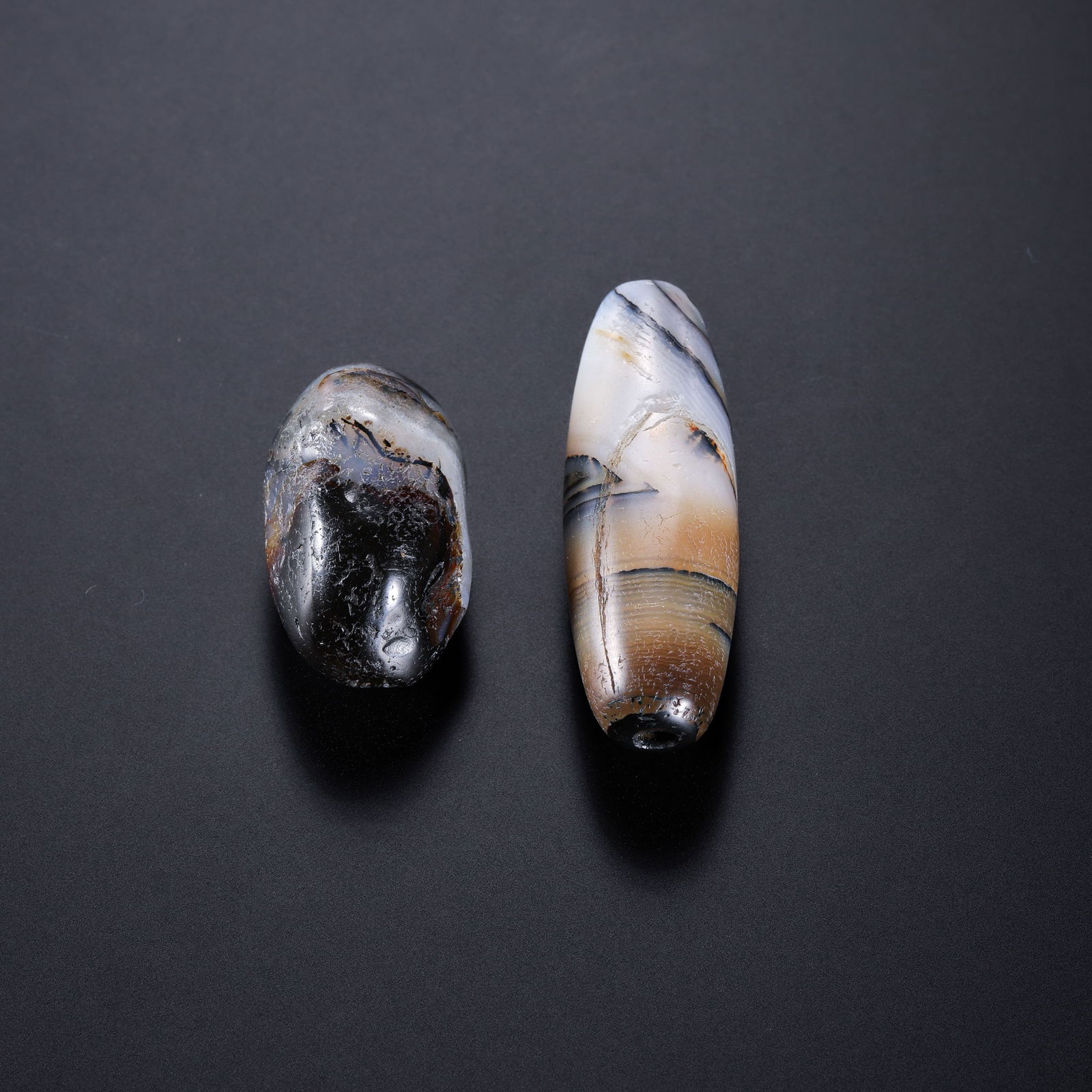 A RARE PAIR OF HIMALAYAN BLACK AND WHITE BANDED AGATE BEADS (SULEMANI)HIMALAYAN REGION, ANCIENT TO: Description This exceptional pair of Banded Agate Beads, traditionally revered in the Himalayan region, is masterfully shaped into elongated spindle forms (gan-zhuan). The stones are characterized by