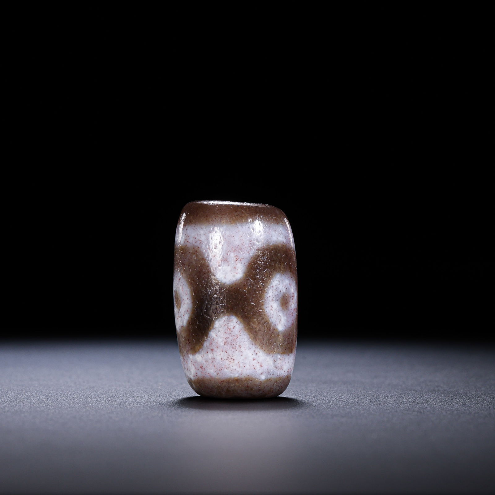 A RARE AND MONUMENTAL 'THREE-EYED' DALO DZI BEADHIMALAYAN REGION, TIBET, ANCIENT TO MEDIEVAL PERIOD: Description This exceptional Dalo Dzi bead is masterfully crafted from premium silicate agate. Unlike the more common elongated spindle-shaped beads, this specimen features a robust, spherical to barr