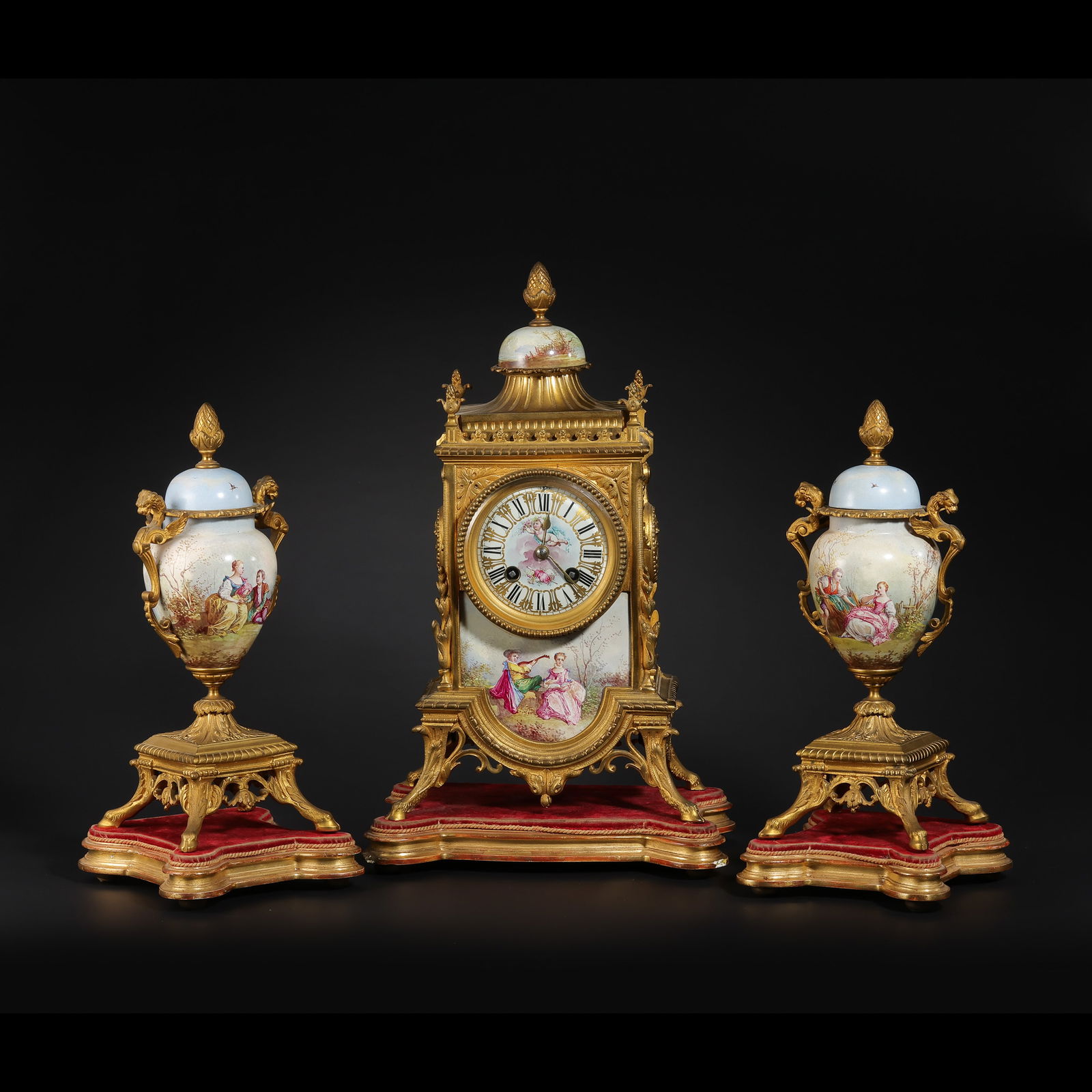 A MAGNIFICENT FRENCH GILT-BRONZE AND PAINTED ENAMEL THREE-PIECE CLOCK GARNITUREPROBABLY PARIS,: Description This opulent three-piece garniture set comprises a central mechanical mantel clock and a flanking pair of matching covered urns (vases). The entire set is masterfully cast in gilt-bronze (