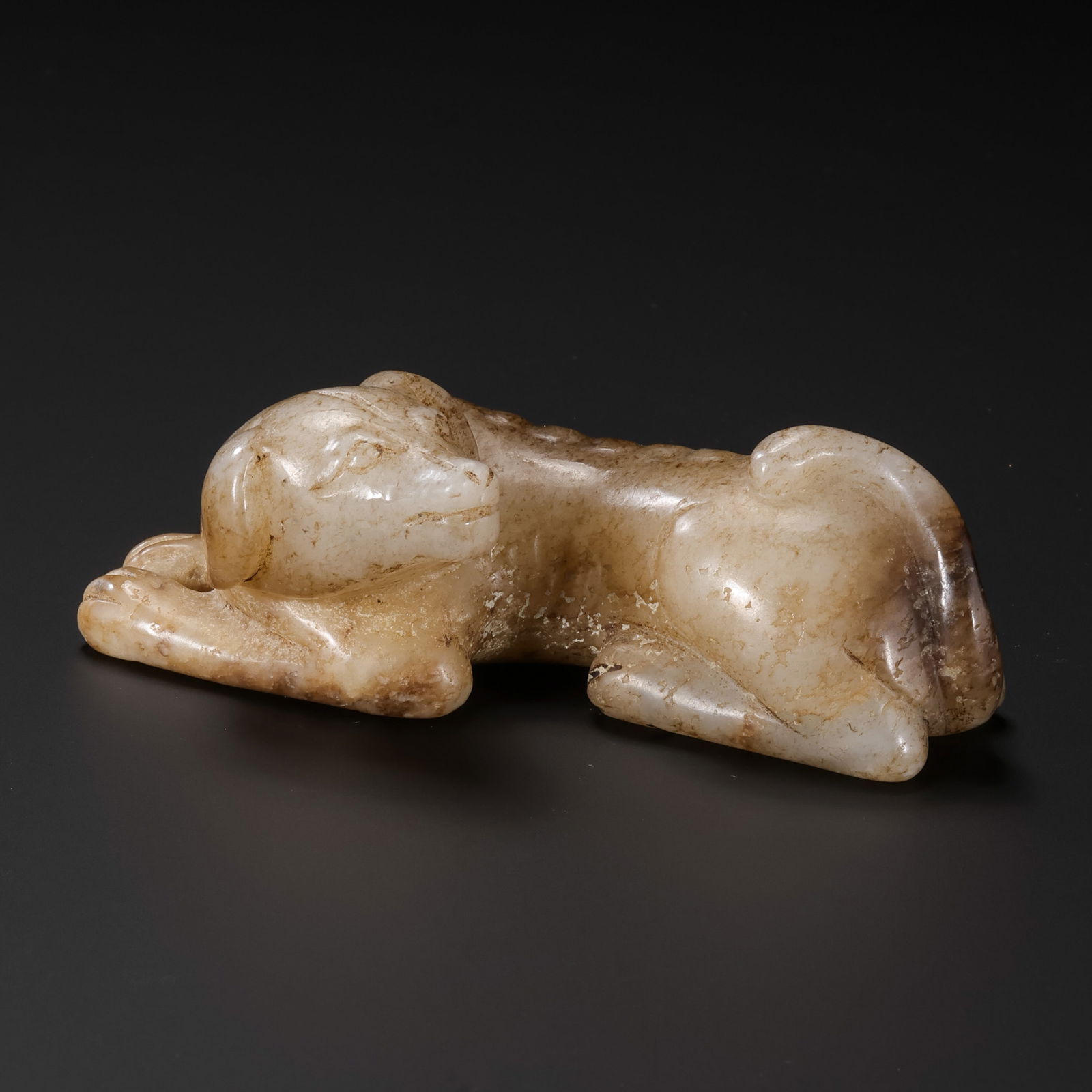 A RARE AND EXPRESSIVE WHITE JADE RECLINING HOUNDHAN DYNASTY OR EARLIER (C. 3RD CENTURY BC – 2ND: Description This exceptionally charming jade carving depicts a faithful hound (wo-quan) in a restful, reclining posture. Carved from a single block of Hetian white jade, the stone has acquired a profo