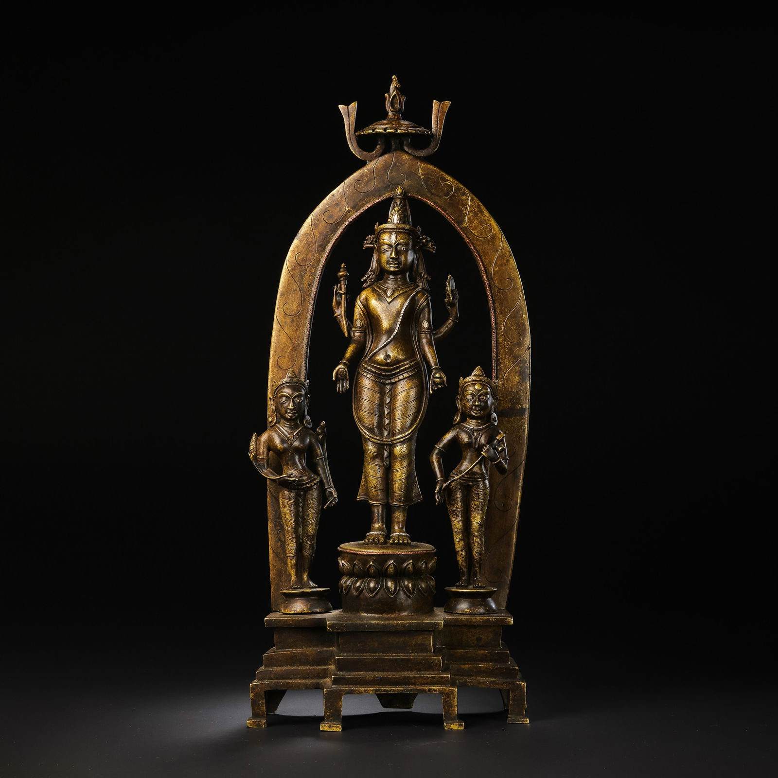 A MAGNIFICENT COPPER ALLOY TRIAD OF A FOUR-ARMED DEITY AND ATTENDANTSCENTRAL TIBET OR NEPAL,: Description This monumental and complex bronze casting represents a pinnacle of Himalayan Buddhist art. The ensemble consists of a central four-armed figure (likely Avalokiteshvara or a form of Maitre