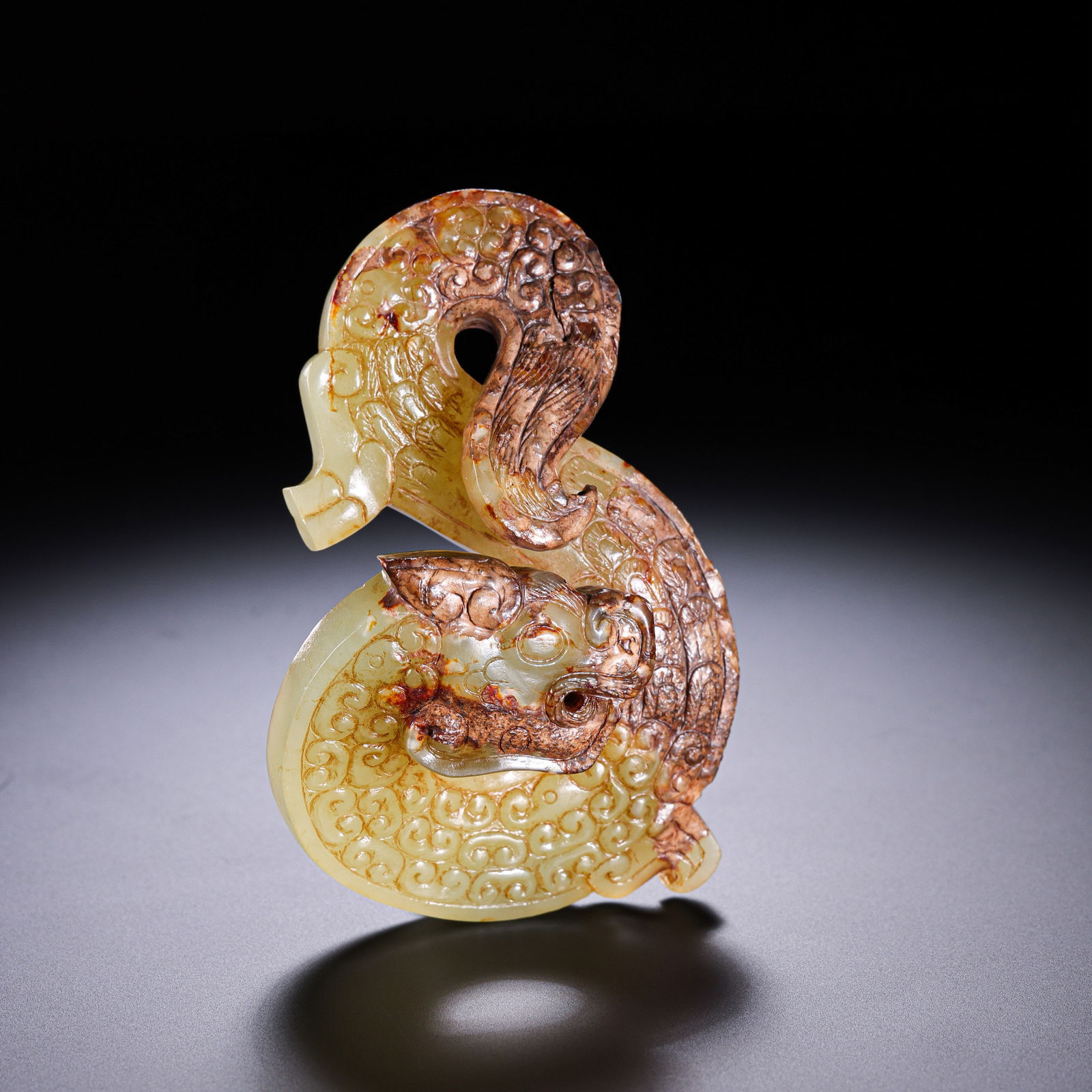 A RARE AND IMPORTANT YELLOW JADE S-SHAPED DRAGONNEOLITHIC PERIOD TO WESTERN ZHOU DYNASTY (C.: Description This monumental jade dragon is carved from a substantial and dense variety of yellow nephrite jade (huang-yu). The stone exhibits a remarkable duality: one half of the dragon's body retain