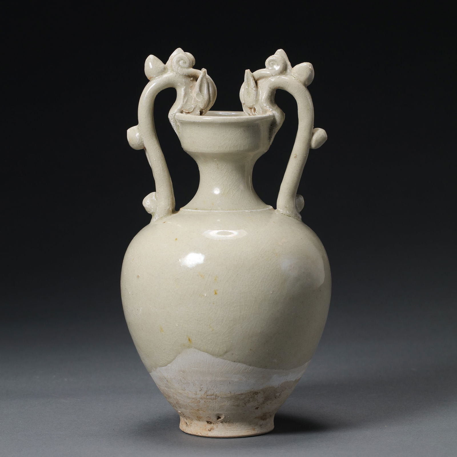 A RARE AND ELEGANT WHITE-GLAZED 'DING' WARE DOUBLE-DRAGON HANDLED AMPHORAFIVE DYNASTIES TO LIAO: Description The amphora is exquisitely potted with an ovoid body tapering to a spreading foot, surmounted by a slender, waisted neck and a flaring 'cup-shaped' mouth. It is flanked by a pair of elegan