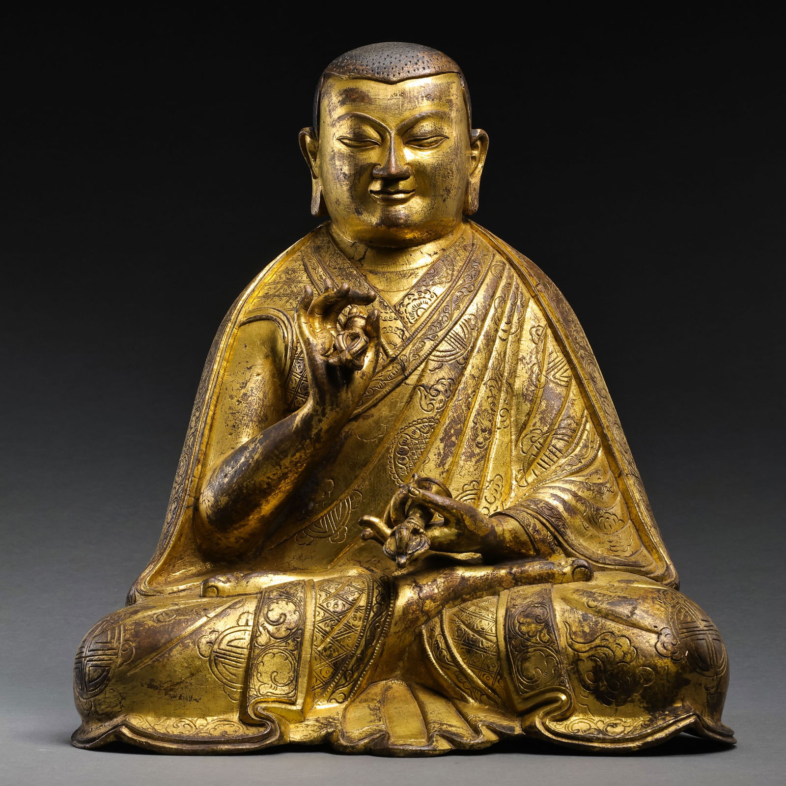 RARE AND MAGNIFICENT GILT-BRONZE FIGURE OF A SEATED LAMATIBET OR NEPAL, 15TH - 16TH CENTURY: DescriptionThe figure is masterfully cast as a revered master, possibly a high-ranking Lama of the Sakya or Gelug school. The countenance is rendered with a striking degree of naturalism, featuring do