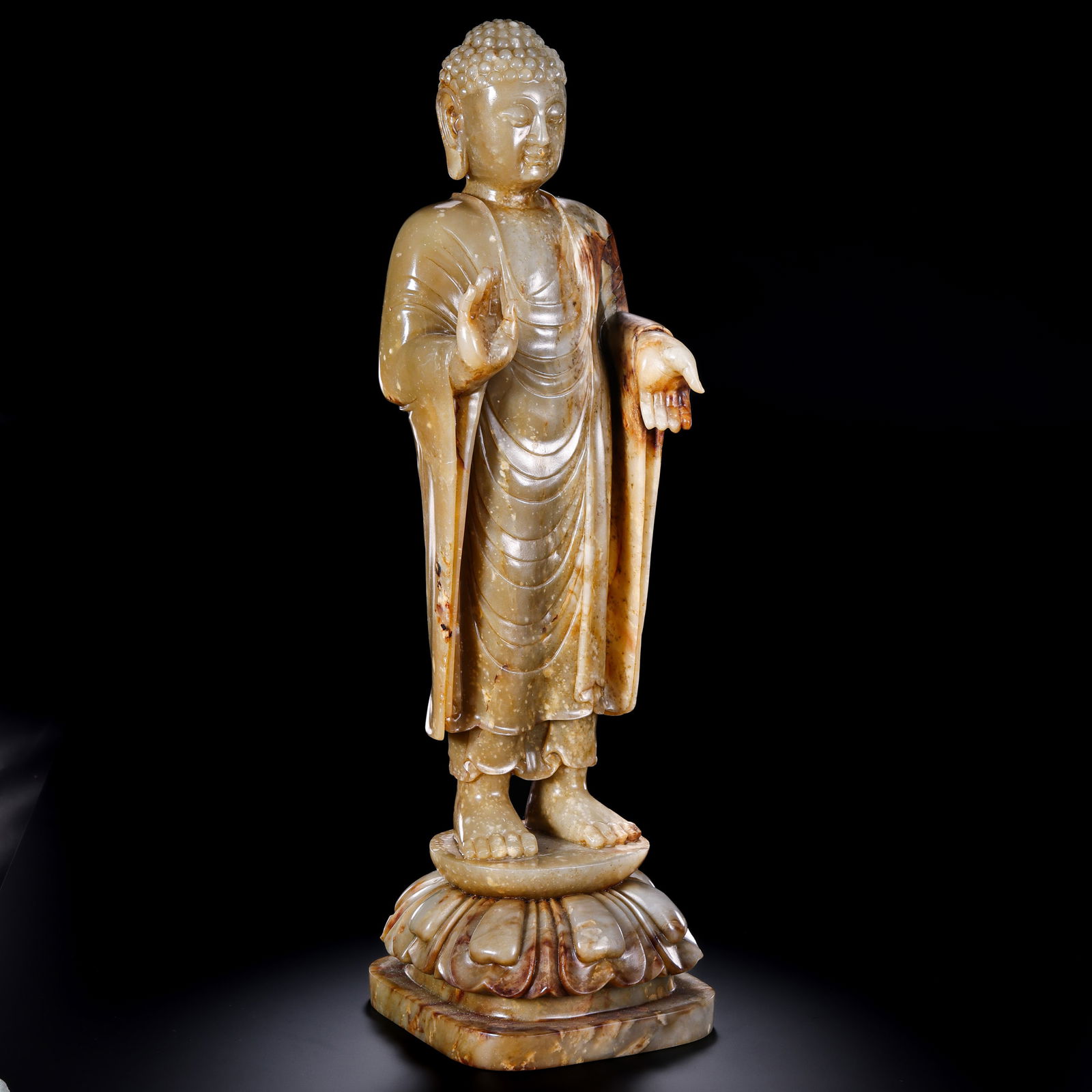 A RARE AND MONUMENTAL WHITE JADE FIGURE OF A STANDING BUDDHAMING DYNASTY (1368–1644) OR EARLIER: Description This magnificent and imposing statue is masterfully carved from a single, exceptionally large block of Hetian nephrite jade. The stone possesses a semi-translucent, pale celadon-white tone