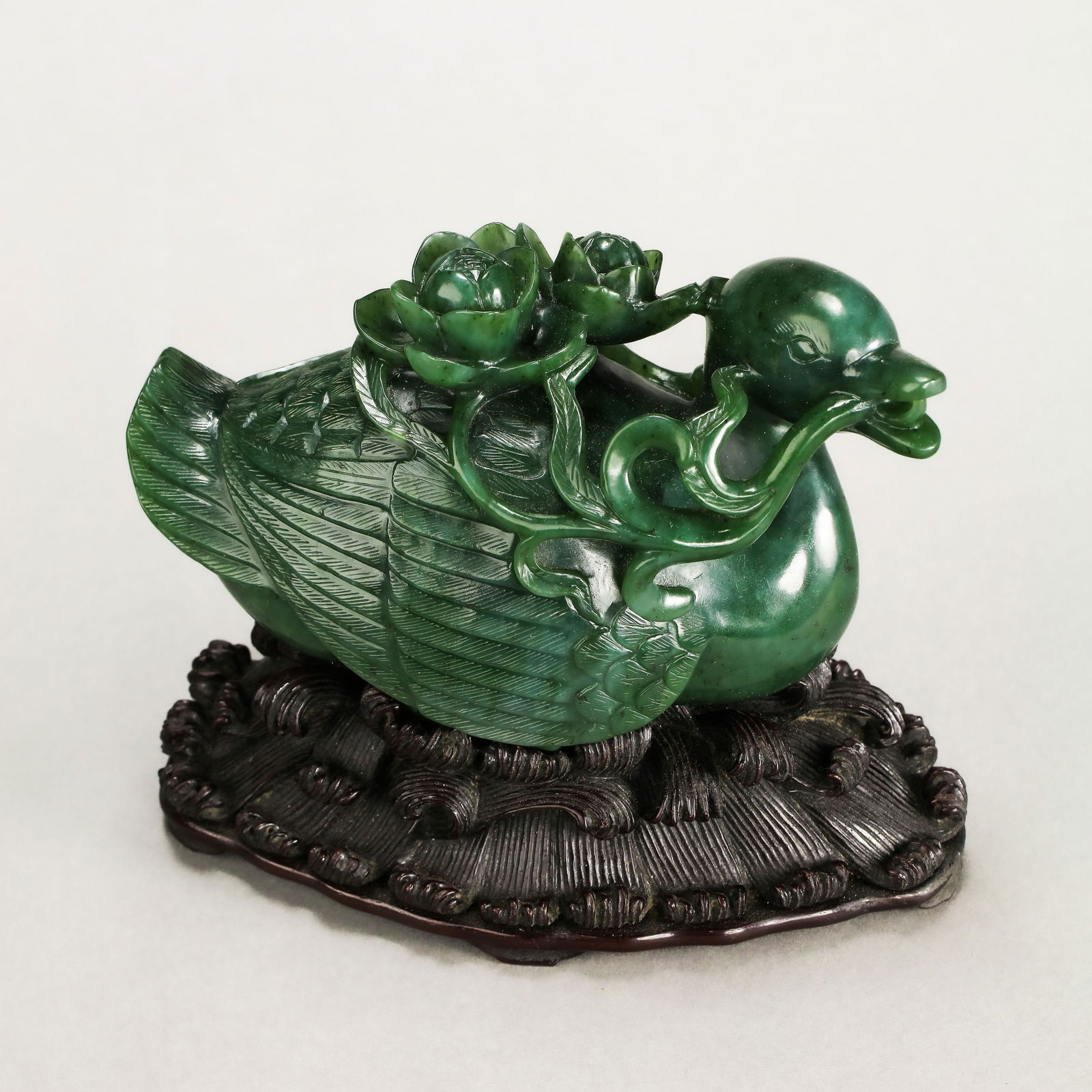 A RARE AND FINELY CARVED SPINACH-GREEN JADE 'LOTUS AND DUCK' GROUPQING DYNASTY, QIANLONG PERIOD: Description The group is masterfully carved from a substantial and exceptionally vibrant spinach-green Hetian jade (nephrite), depicting a plump, well-proportioned duck in a resting posture. The duck'