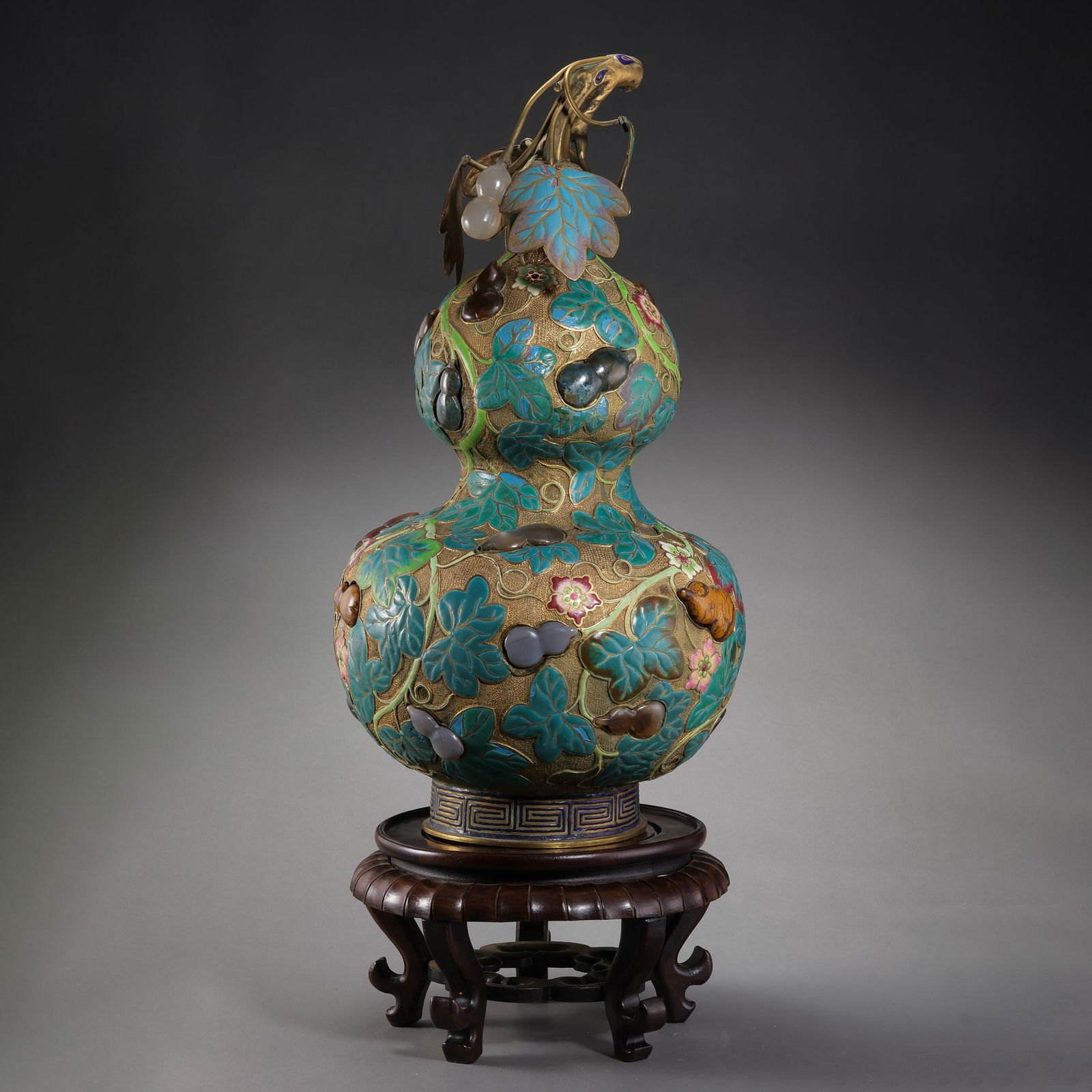 A RARE AND MAGNIFICENT IMPERIAL GILT-BRONZE AND CLOISONNÉ ENAMEL 'MULTI-TREASURE' DOUBLE-GOURD: Description The vase is expertly fashioned in the auspicious form of a double-gourd (hulu), symbolizing longevity and prosperity. The body is constructed from heavily gilt-bronze (liu-jin), with the p