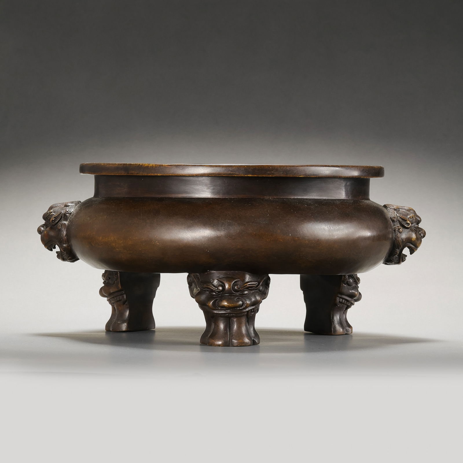 A RARE AND IMPRESSIVELY CAST BRONZE 'LION-MASK' TRIPOD CENSERMARK OF XUANDE, MING DYNASTY: Description This substantial and masterfully cast bronze censer is of tripod Ge form, featuring a compressed globular body supported by three robust mythical beast-mask feet (shou-zu). The vessel is f