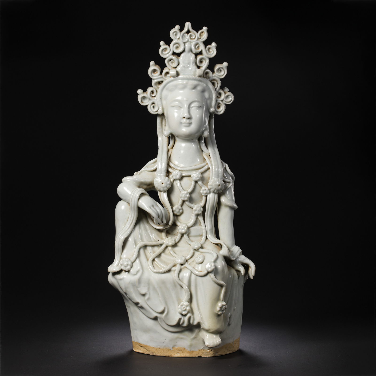 A MAGNIFICENT AND RARE WHITE-GLAZED FIGURE OF A SEATED GUANYINSONG DYNASTY (960–1279): The figure is exquisitely modeled as the Bodhisattva Guanyin, seated in the position of royal ease (rajalilasana). The face is rendered with an ethereal serenity, featuring narrow downcast eyes beneat