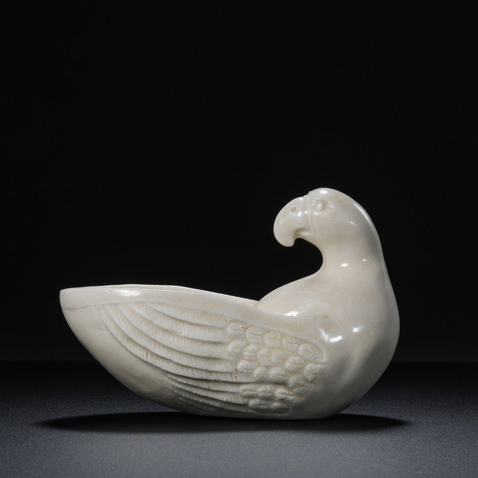 A RARE AND CHARMING WHITE-GLAZED 'PARROT' CUPTANG – FIVE DYNASTIES (9TH – 10TH CENTURY): The cup is imaginatively modeled in the form of a reclining parrot, the bird's hollowed body forming the vessel's basin. The parrot is depicted with its head turned back over its wing, its hooked beak