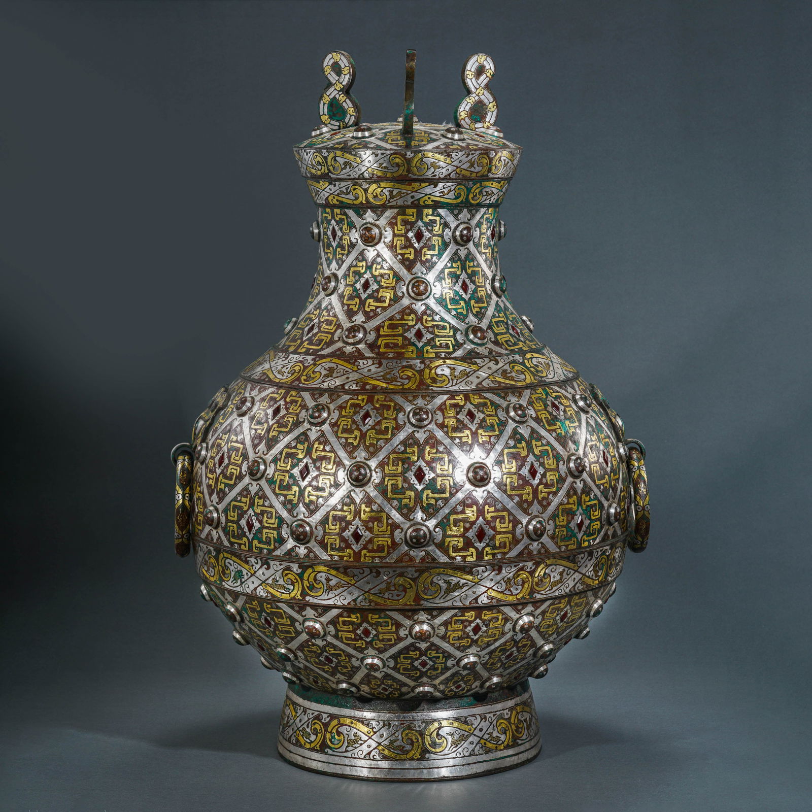 A MAGNIFICENT AND MONUMENTAL GOLD AND SILVER-INLAID BRONZE CAPPED VASE, 'HU'WARRING STATES PERIOD: Description The vessel is of imposing proportions and masterfully cast, featuring a pear-shaped body rising from a flared foot to a waisted neck and a fitted domed cover. The exterior is sumptuously d