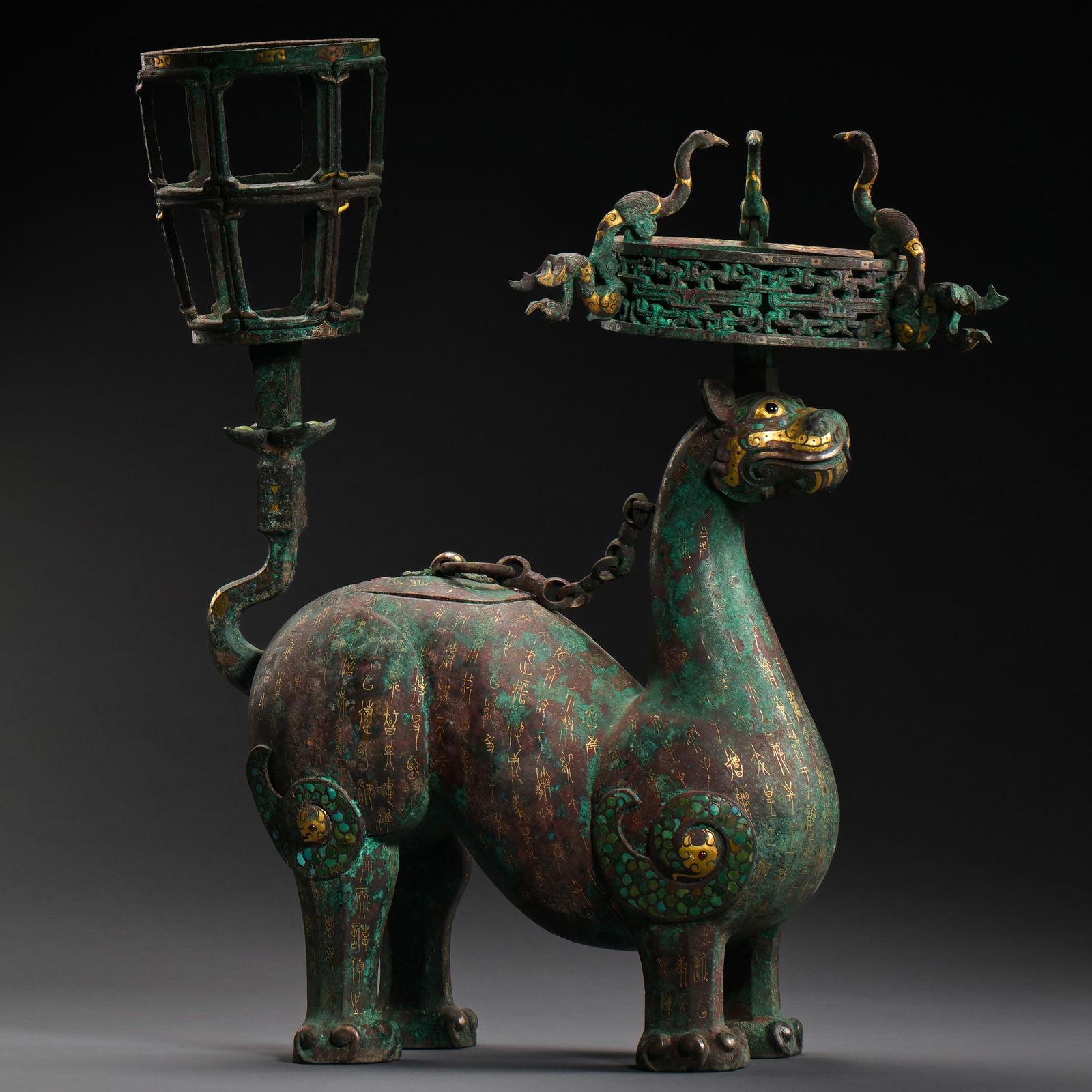 AN EXTREMELY RARE AND MAGNIFICENT GOLD AND SILVER-INLAID BRONZE 'MYTHICAL BEAST' LAMP STANDWARRING: The bronze lamp stand is an engineering and artistic marvel of the late Bronze Age. It features a wide, circular oil tray supported by a tall, slender central fluted column. The base is masterfully ca