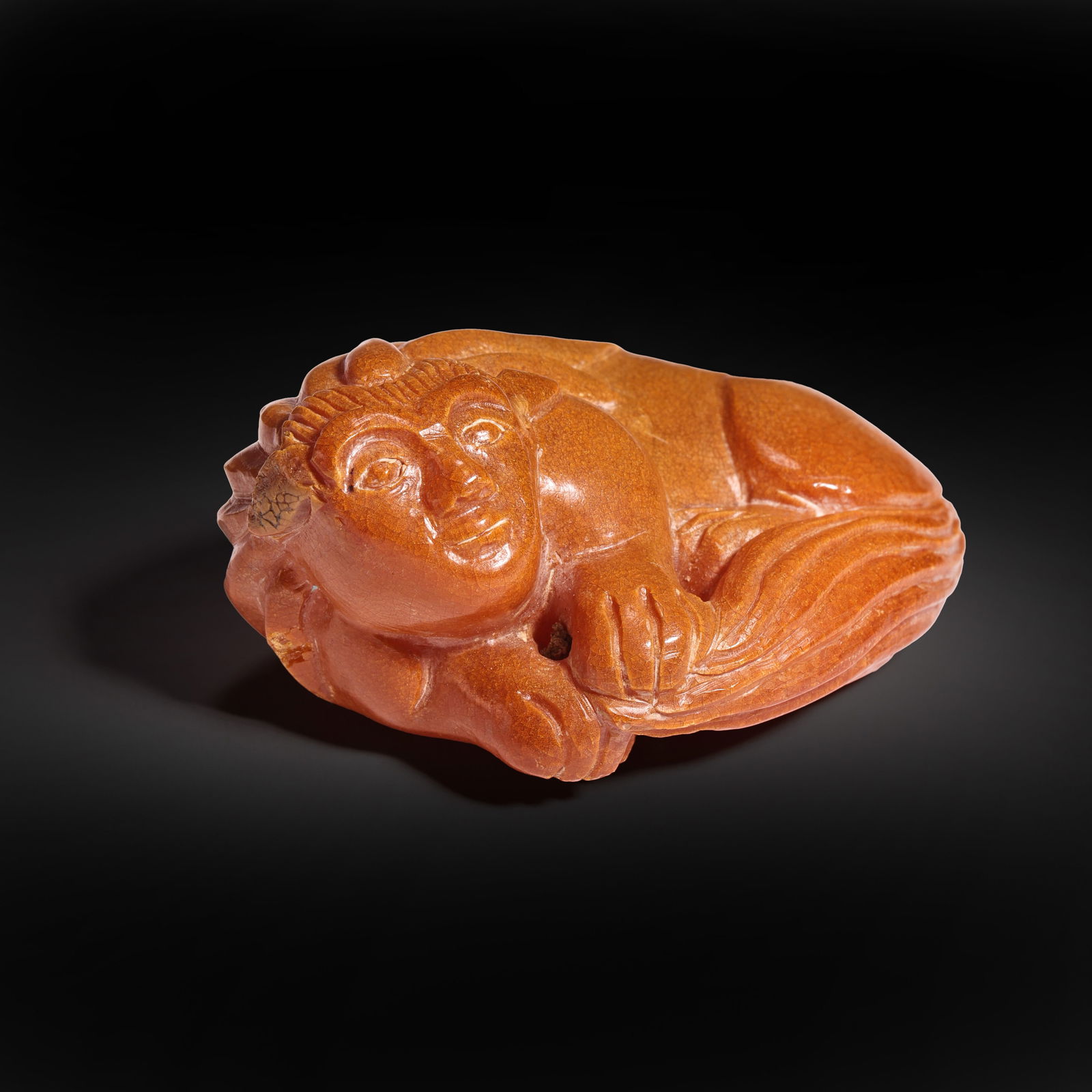 A RARE AMBER 'SPHINX' PENDANTTANG - LIAO DYNASTY (618-1125): The pendant is masterfully carved from a single piece of amber, depicting a sphinx-like winged creature with a human head and a feline body. The material displays a deep honey-colored hue with rich re
