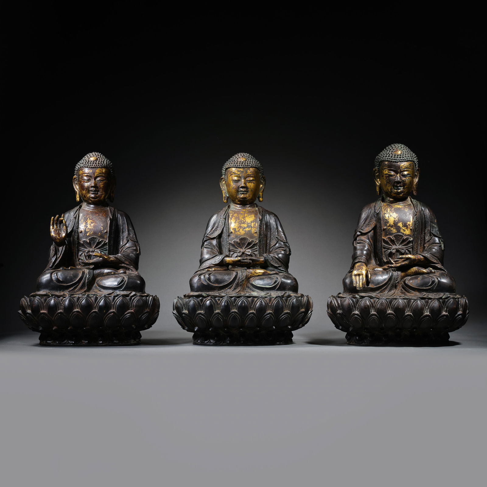 A RARE AND MAGNIFICENT SET OF THREE GILT-BRONZE FIGURES OF THE BUDDHAS OF THE THREE TIMESMING: Description The set comprises three masterfully cast seated figures representing the Buddhas of the Three Times: Shakyamuni (the Buddha of the Present), Dipamkara (the Buddha of the Past), and Maitrey