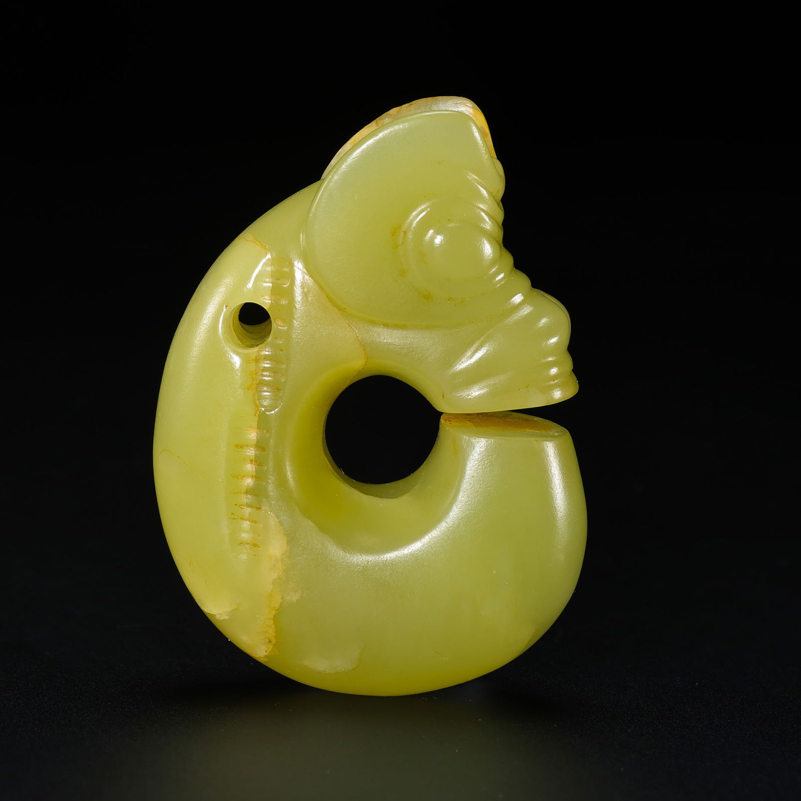 A RARE AND IMPORTANT YELLOW JADE 'ZHULONG' (PIG-DRAGON)NEOLITHIC PERIOD, HONGSHAN CULTURE (C.: The ritual ornament is masterfully carved from an enticing pale yellowish-celadon jade with areas of opaque russet and cloudy white calcification, consistent with long-term burial. The "pig-dragon" is