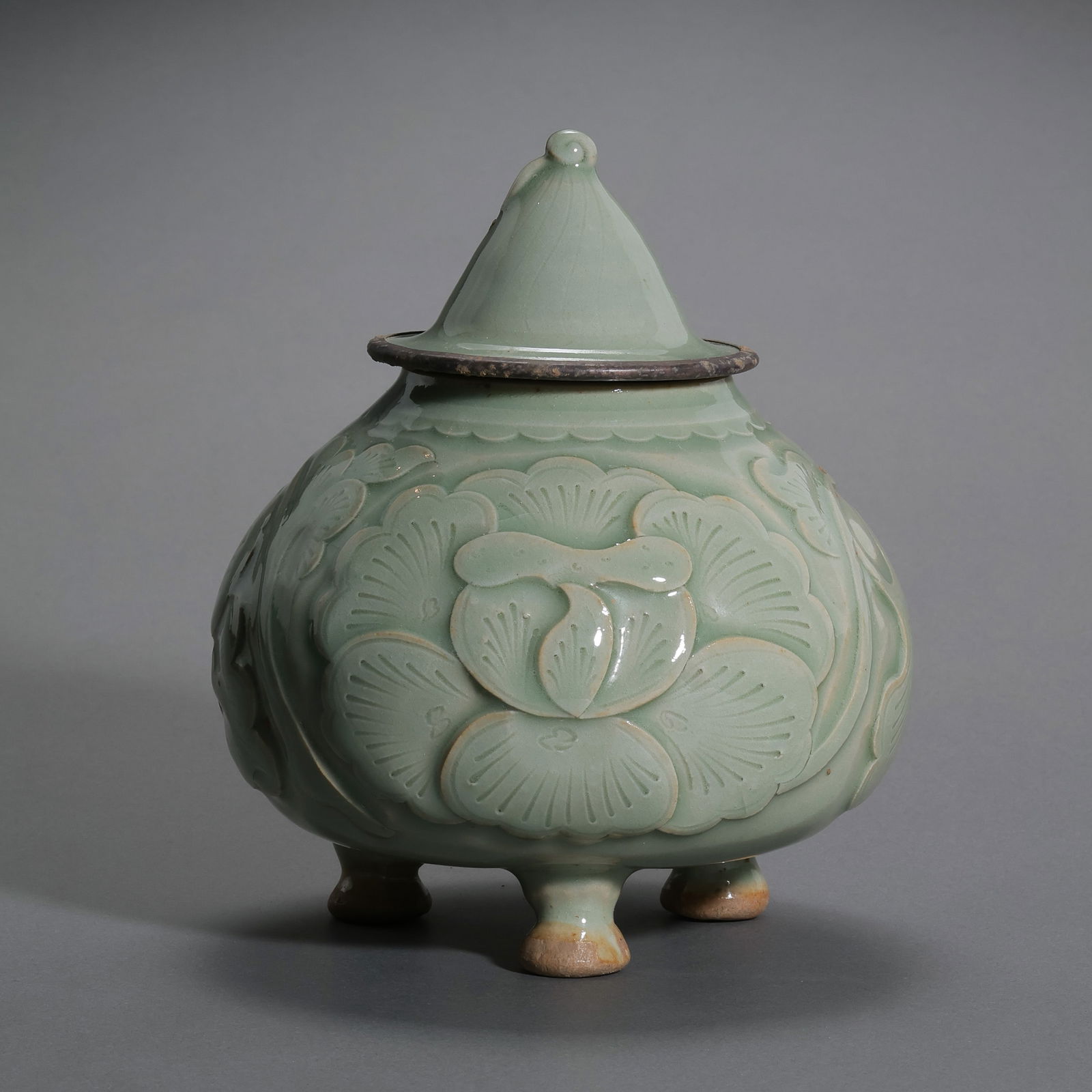 A RARE AND EXQUISITE 'MI-SE' YUE CELADON-GLAZED CARVED 'LOTUS' TRIPOD JAR AND COVERFIVE DYNASTIES TO: Description This exceptionally refined vessel is a masterpiece of Yue ware, representing the technical and aesthetic peak of the 10th-century ceramic tradition. The jar features a compressed globular
