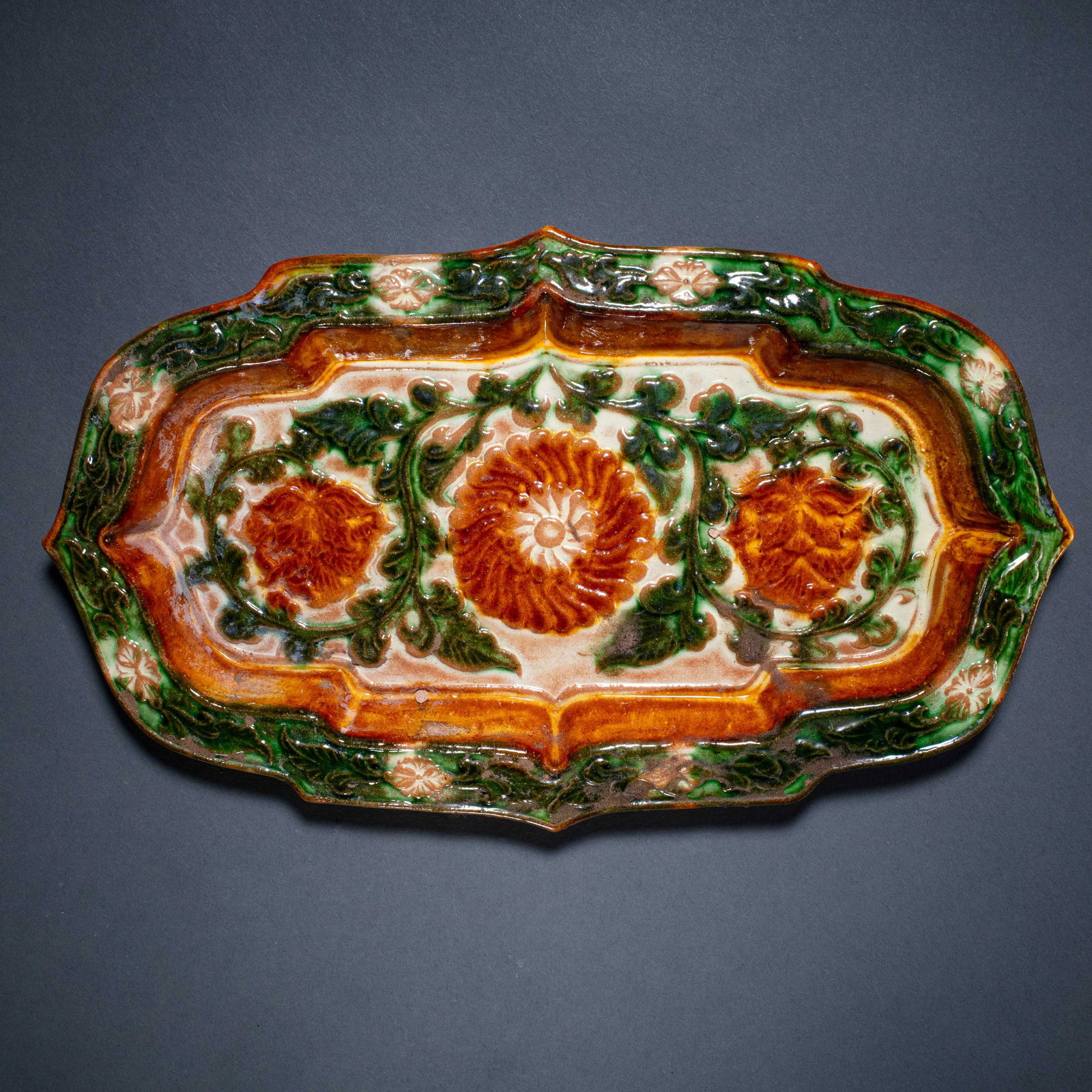 A MAGNIFICENT AND RARE 'SANCAI' GLAZED MOLDED 'FLORAL' DISHTANG DYNASTY (618–907): The dish is of refined form, supported on a short spreading foot, with a broad interior exquisitely decorated in the center with a stylized molded floral medallion. The central blossom is surrounded b