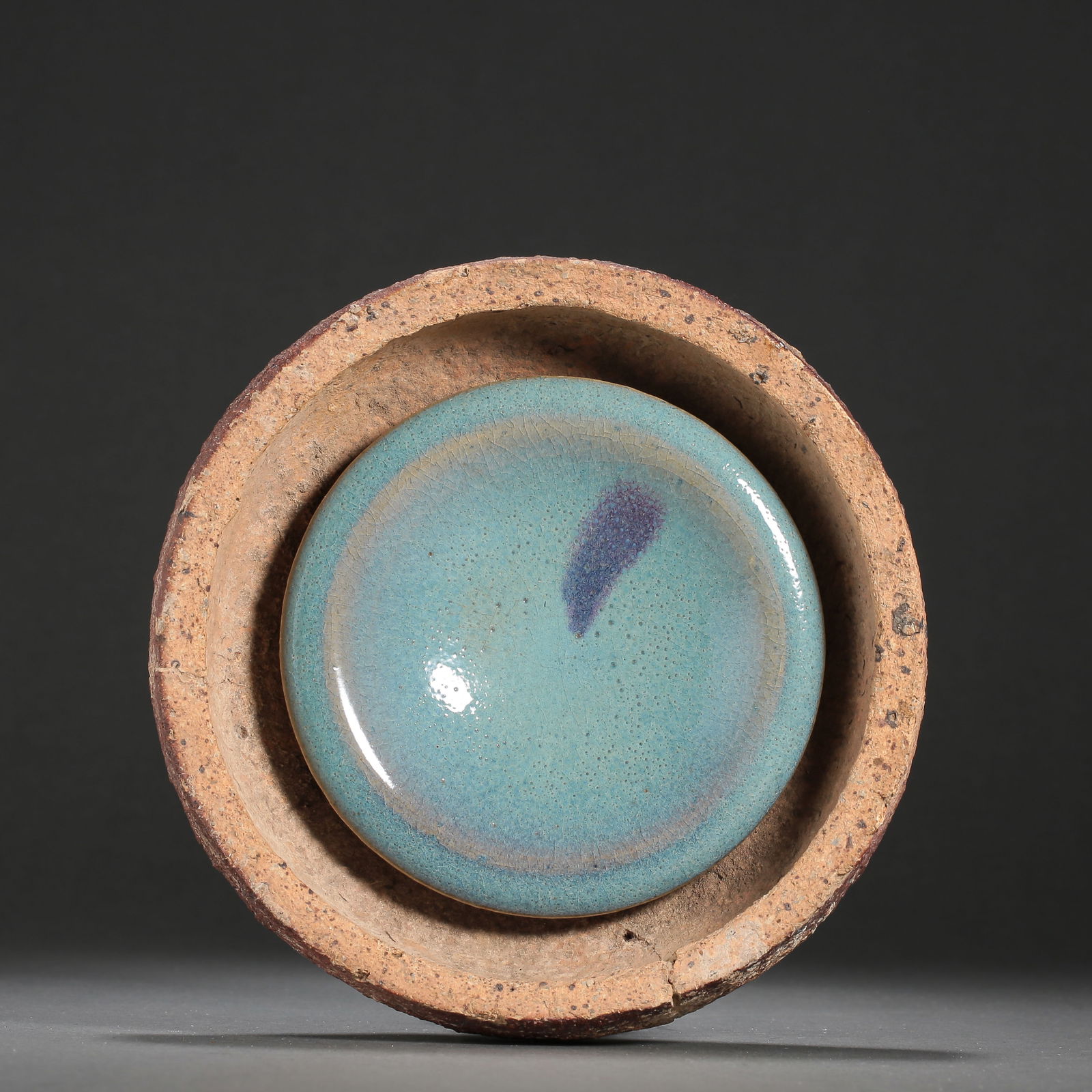 A RARE JUN WARE 'PURPLE-SPLASHED' DISH FUSED IN ITS SAGGARSONG - JIN DYNASTY (960-1234): The dish is covered with a thick, opalescent sky-blue glaze thinning to a mushroom tone at the rim, centered with a vibrant copper-red purple splash. It remains permanently fused to the interior of it