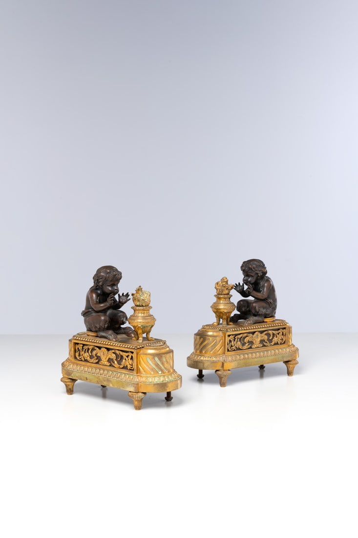 Pair of andirons "aux amours frileux" in chased, patinated, and gilded bronze, on an oblong base: Pair of andirons "aux amours frileux" in chased, patinated, and gilded bronze, on an oblongbase with acanthus, pearls, gadroons, and waterleaf frieze, with toupie back feet.Late Louis XVIth periodH 23